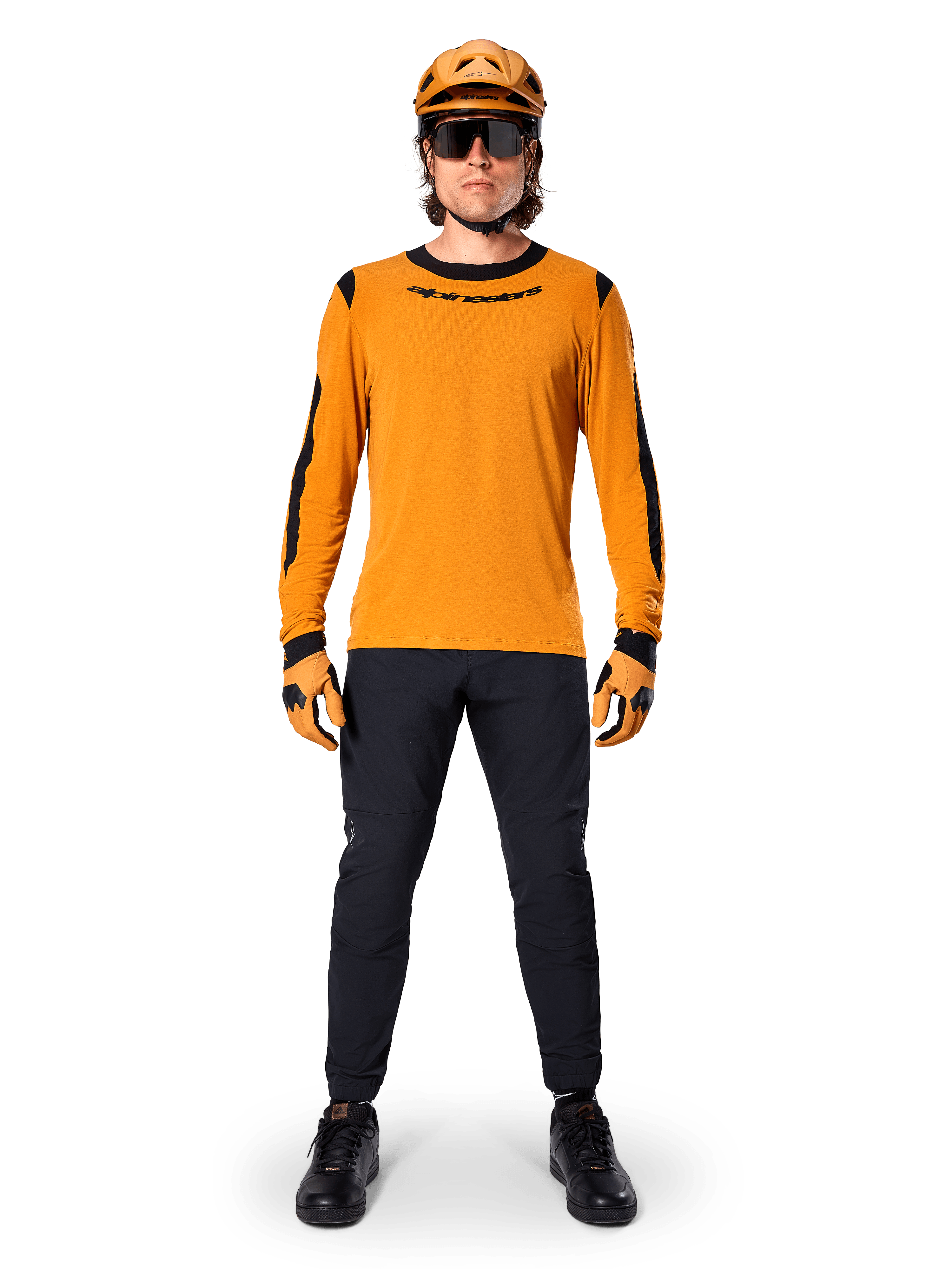 Mountainbiker im Alpinestars A-Dura Dri Wool Langarmtrikot, Dunkelgold mit schwarzen Akzenten an Kragen und Ärmeln, kombiniert mit einer schwarzen Hose, passendem goldenem Helm, Handschuhen und einer schwarzen Sonnenbrille, professionelle Mountainbike-Ausrüstung