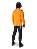 Mountainbiker von hinten gesehen im Alpinestars A-Dura Dri Wool Langarmtrikot in Dark Gold, schwarze technische Hose mit weißem Branding und passendem schwarz-orangenem Helm, leistungsorientierte Mountainbike-Bekleidung.