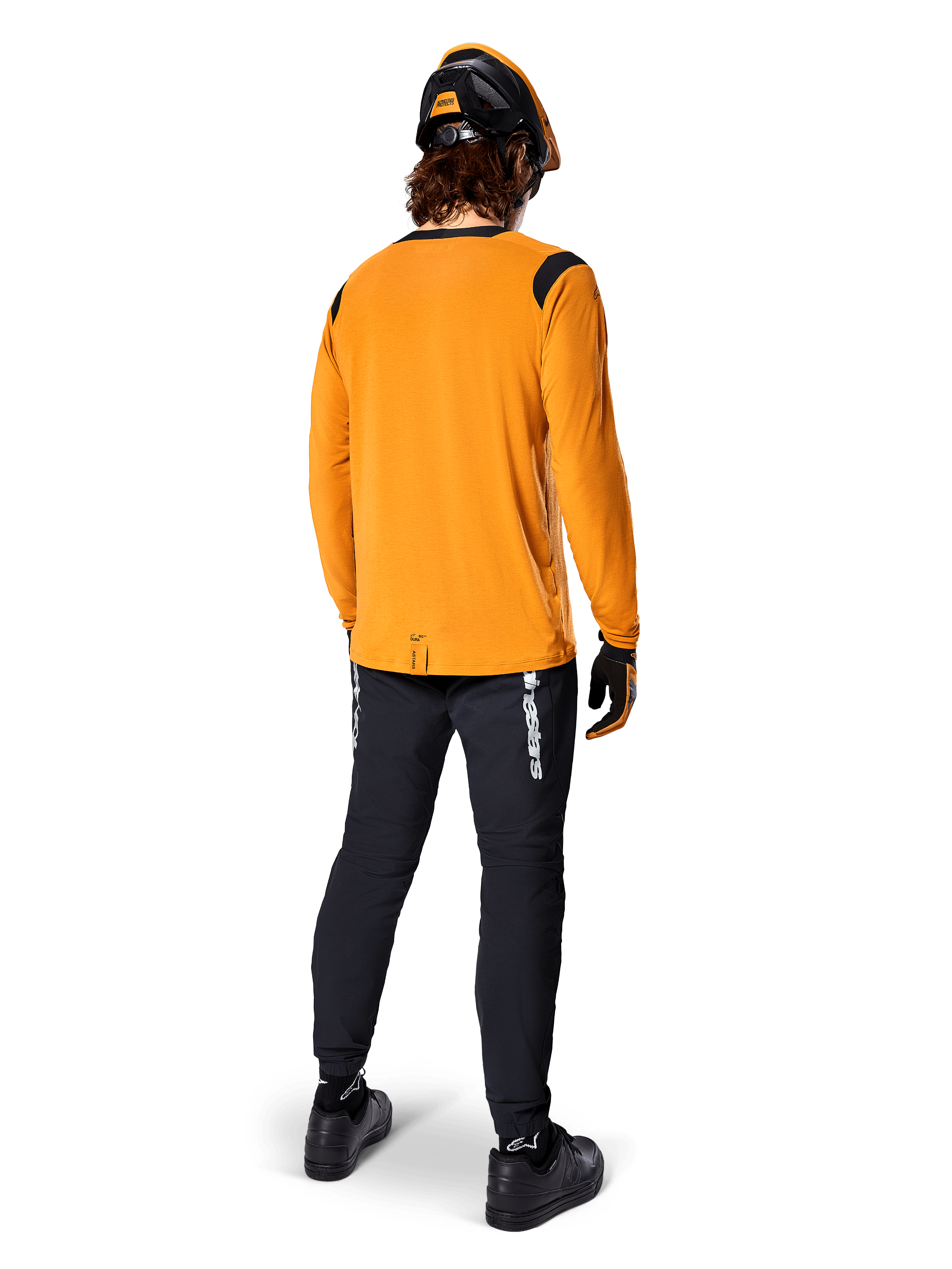 Mountainbiker von hinten gesehen im Alpinestars A-Dura Dri Wool Langarmtrikot in Dark Gold, schwarze technische Hose mit weißem Branding und passendem schwarz-orangenem Helm, leistungsorientierte Mountainbike-Bekleidung.