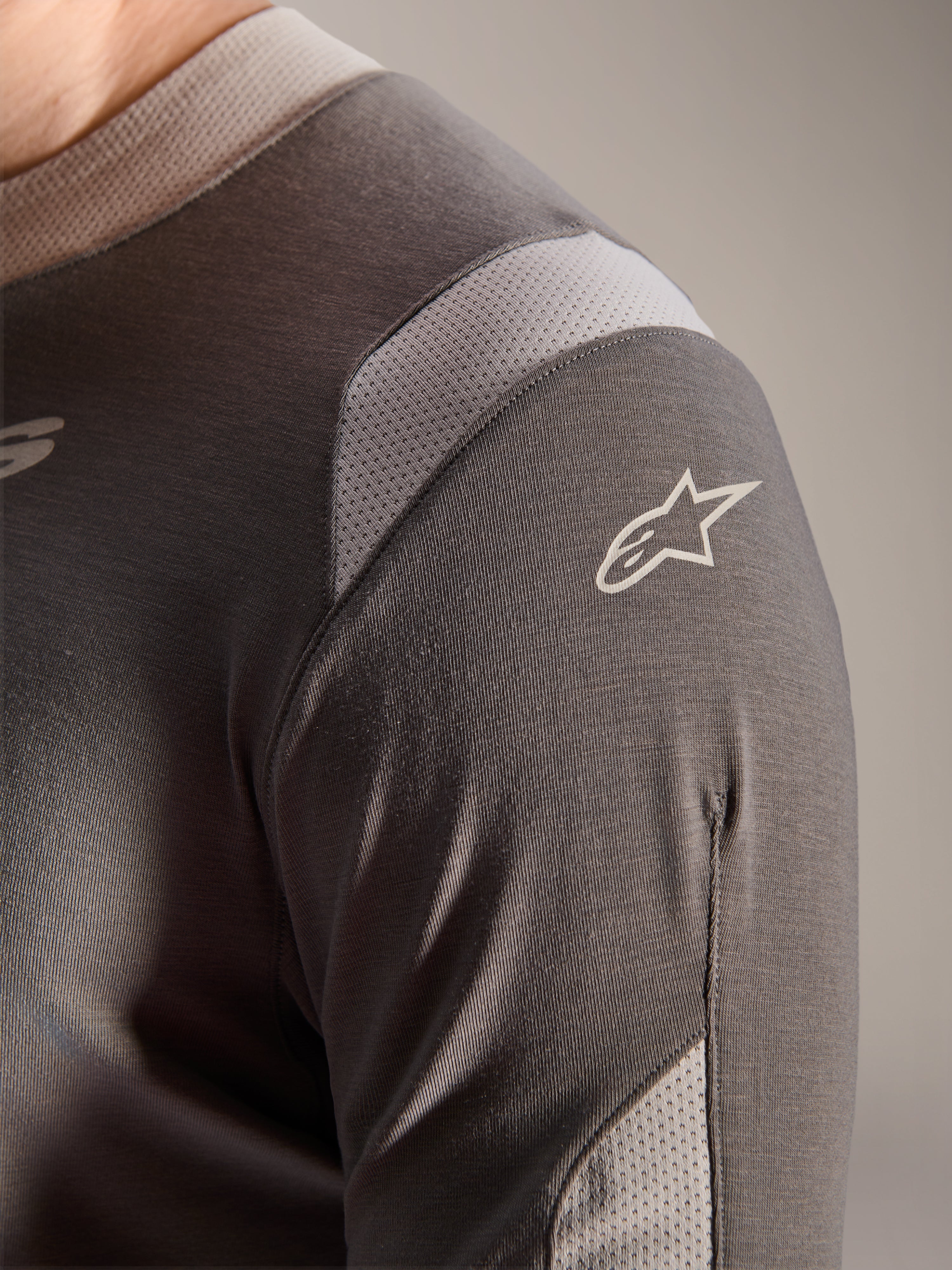 Alpinestars A-Dura Dri Wool Langarmtrikot, Dunkelgrau, Detailansicht der Schulter und des Ärmels mit hellgrauen Mesh-Belüftungseinsätzen und weißem Astars-Logo auf dem technischen drirelease-Gewebe.