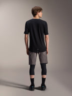 Alpinestars A-Dura Dri Wool Kurzarmtrikot, Schwarz, Rückansicht getragen von einem Modell mit grauen MTB-Shorts und schwarzen Knieschützern, mit längerem Rückensaum und athletischer Passform für den Offroad-Radsport
