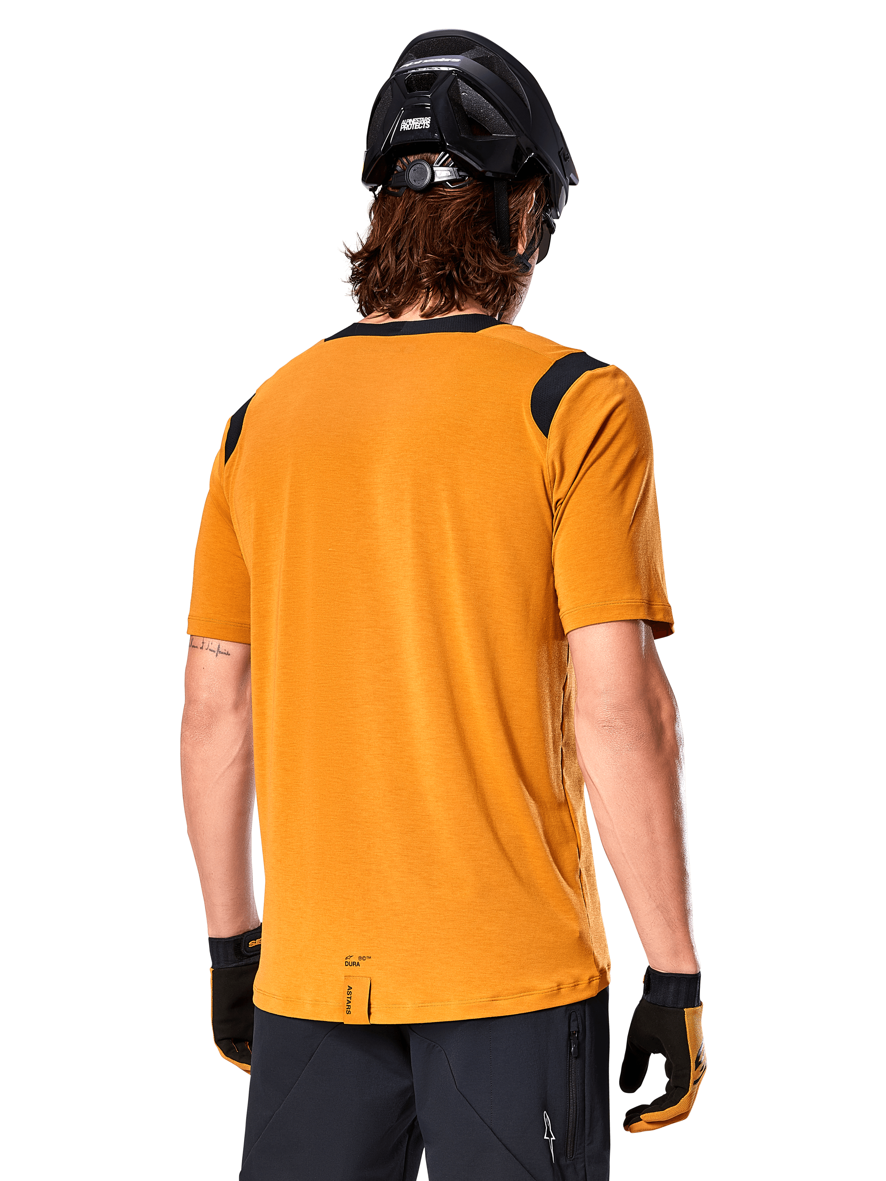 Alpinestars A-Dura Dri Wool Kurzarmtrikot, Dunkelgold, Rückansicht eines Mannes, der das Trikot mit schwarzen Mesh-Einsätzen an den Schultern trägt, kombiniert mit schwarzem MTB-Helm und Handschuhen, MTB-Ausrüstung in regulärer Passform