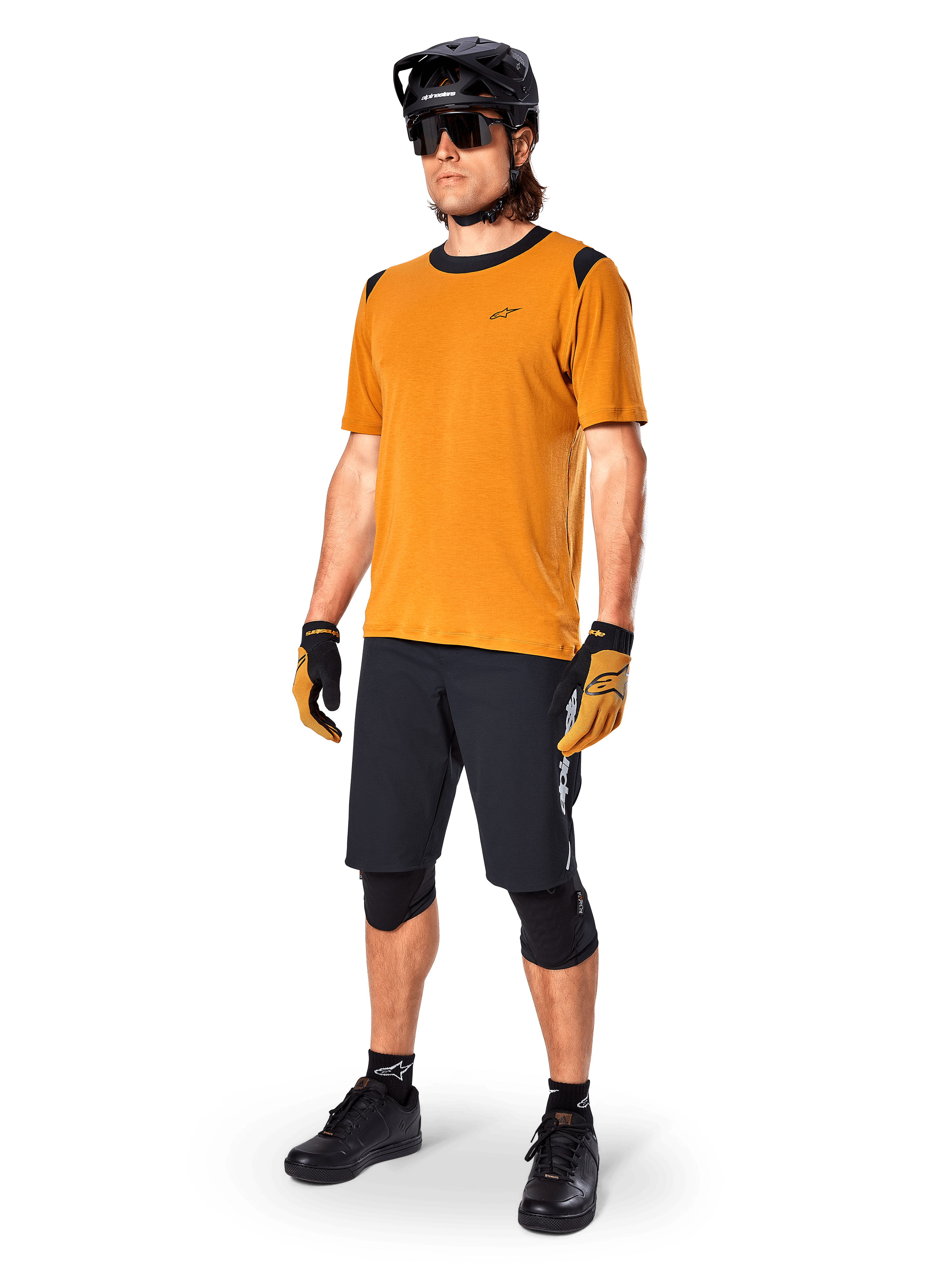 Männliches Model im Alpinestars A-Dura Dri Wool Kurzarmtrikot in Dark Gold, Mountainbike-Trikot mit schwarzen Schulter- und Kragenakzenten, kombiniert mit schwarzen MTB-Shorts, schwarzem Helm und Sonnenbrille, technische Offroad-Radsportausrüstung