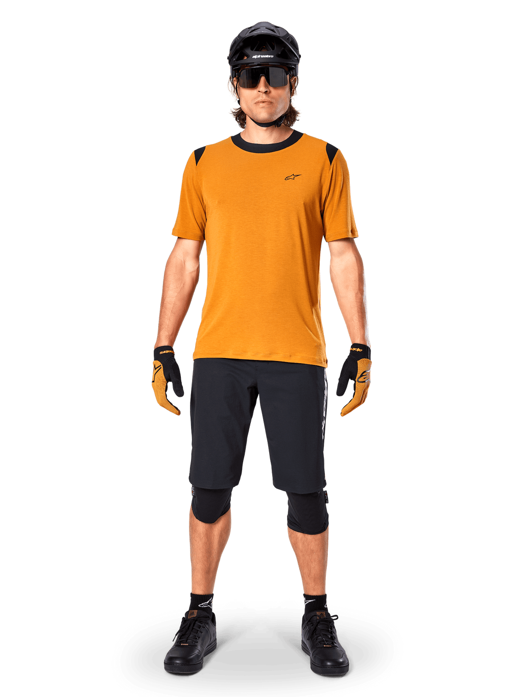 Alpinestars A-Dura Dri Wool Kurzarmtrikot in Dark Gold, Mountainbike-Trikot kombiniert mit schwarzen Shorts und Schutzausrüstung, senfgelbes Material mit schwarzem Kragen und Schulterakzenten, Performance-Radbekleidung für Trail-Fahrten.