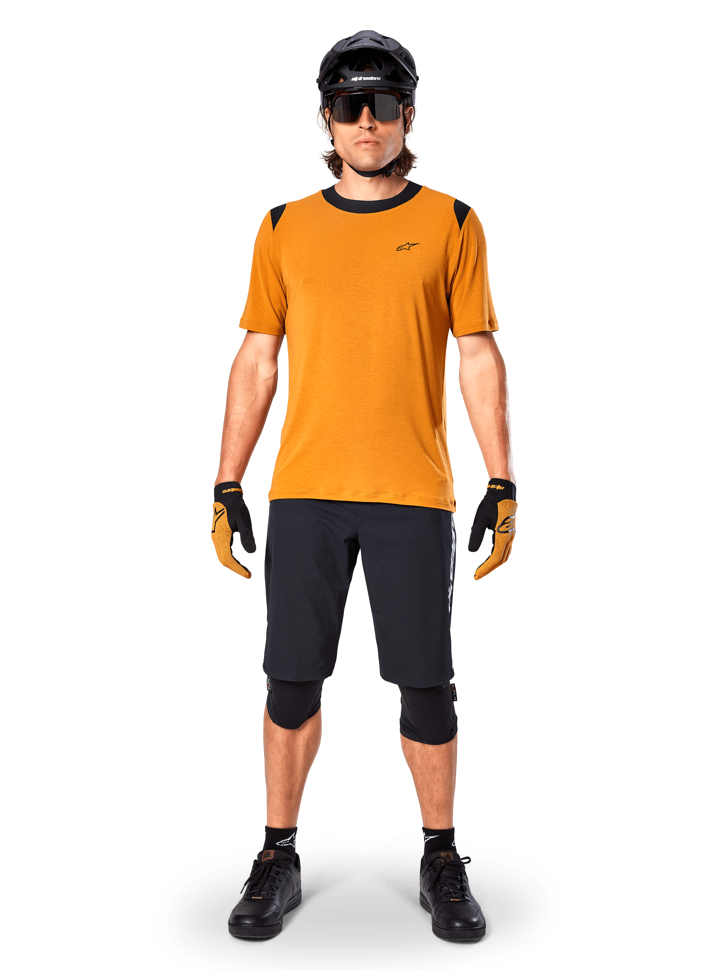 Alpinestars A-Dura Dri Wool Kurzarmtrikot in Dark Gold, Mountainbike-Trikot kombiniert mit schwarzen Shorts und Schutzausrüstung, senfgelbes Material mit schwarzem Kragen und Schulterakzenten, Performance-Radbekleidung für Trail-Fahrten.