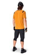 Alpinestars A-Dura Dri Wool Kurzarmtrikot, Radsport-Trikot, Dunkelgold, Rückansicht eines Mountainbikers in senfgelbem Trikot mit schwarzen Mesh-Schulterakzenten, kombiniert mit schwarzen Shorts, Knieschützern, schwarzem Helm und Handschuhen, technische Offroad-Radsportausrüstung
