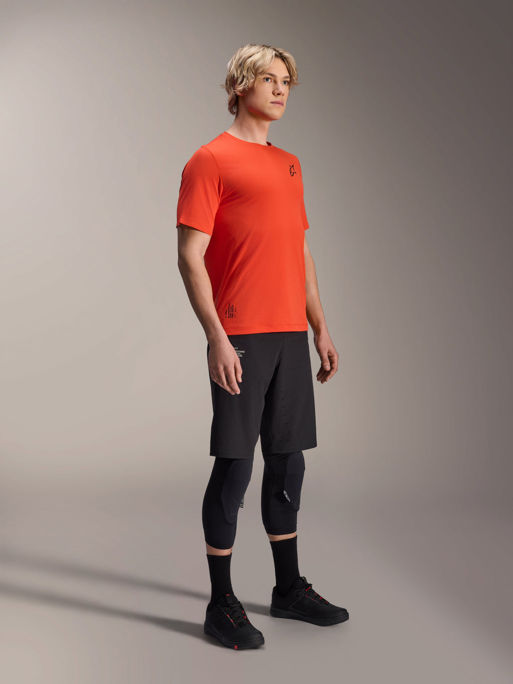 Alpinestars A-Aria Astar Kurzarmtrikot in Spicy Orange, getragen von einem Model mit schwarzen MTB-Shorts und Knieschutz, leichte, atmungsaktive Mountainbike-Bekleidung, kräftiges Orange mit minimalem schwarzem Branding