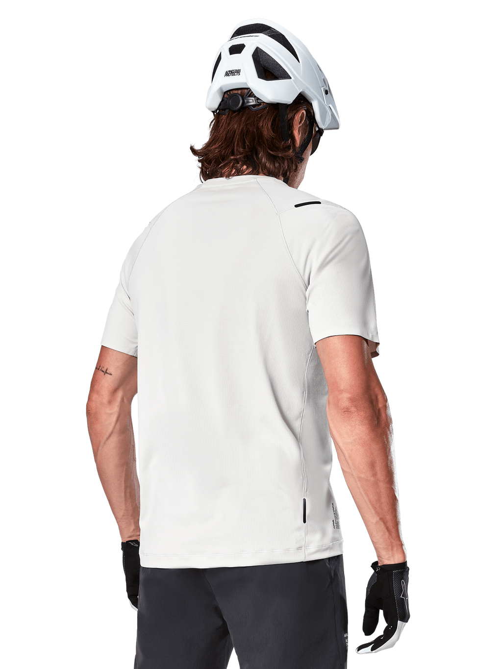 Alpinestars A-Aria Astar Trikot, Kurzarm, White Dove, Rückansicht eines leichten, atmungsaktiven Mountainbike-Trikots, getragen mit einem weißen Helm und schwarzen Fahrradhandschuhen, mit verlängertem Saum für zusätzliche Abdeckung