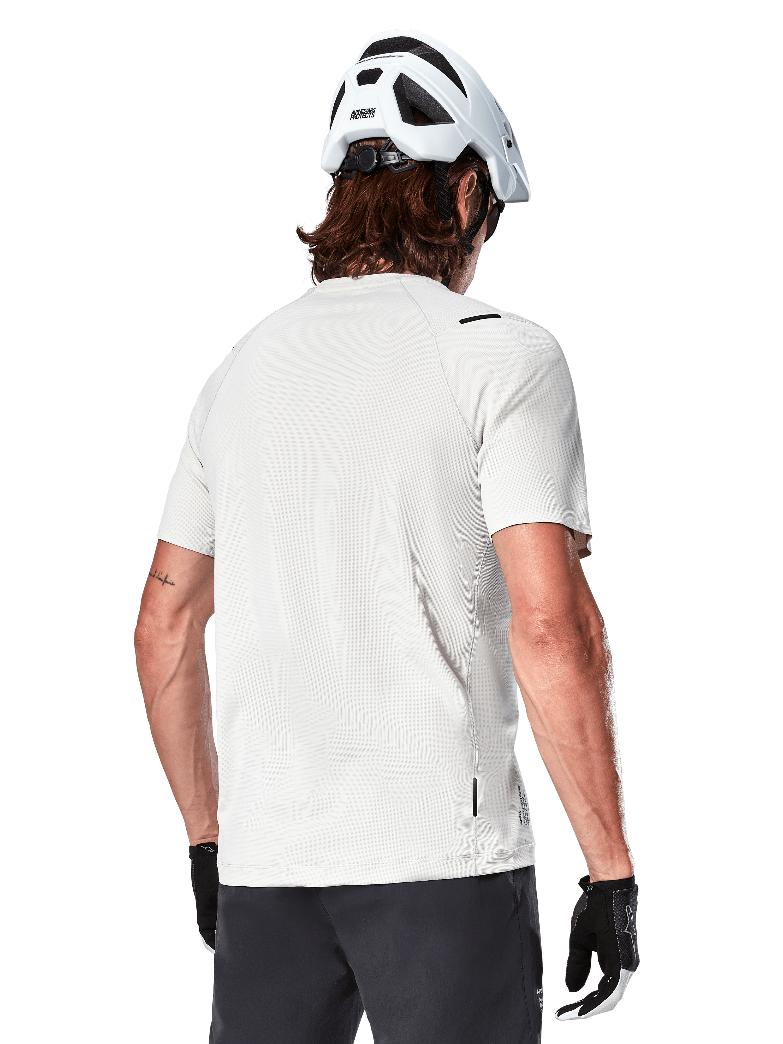 Alpinestars A-Aria Astar Trikot, Kurzarm, White Dove, Rückansicht eines leichten, atmungsaktiven Mountainbike-Trikots, getragen mit einem weißen Helm und schwarzen Fahrradhandschuhen, mit verlängertem Saum für zusätzliche Abdeckung