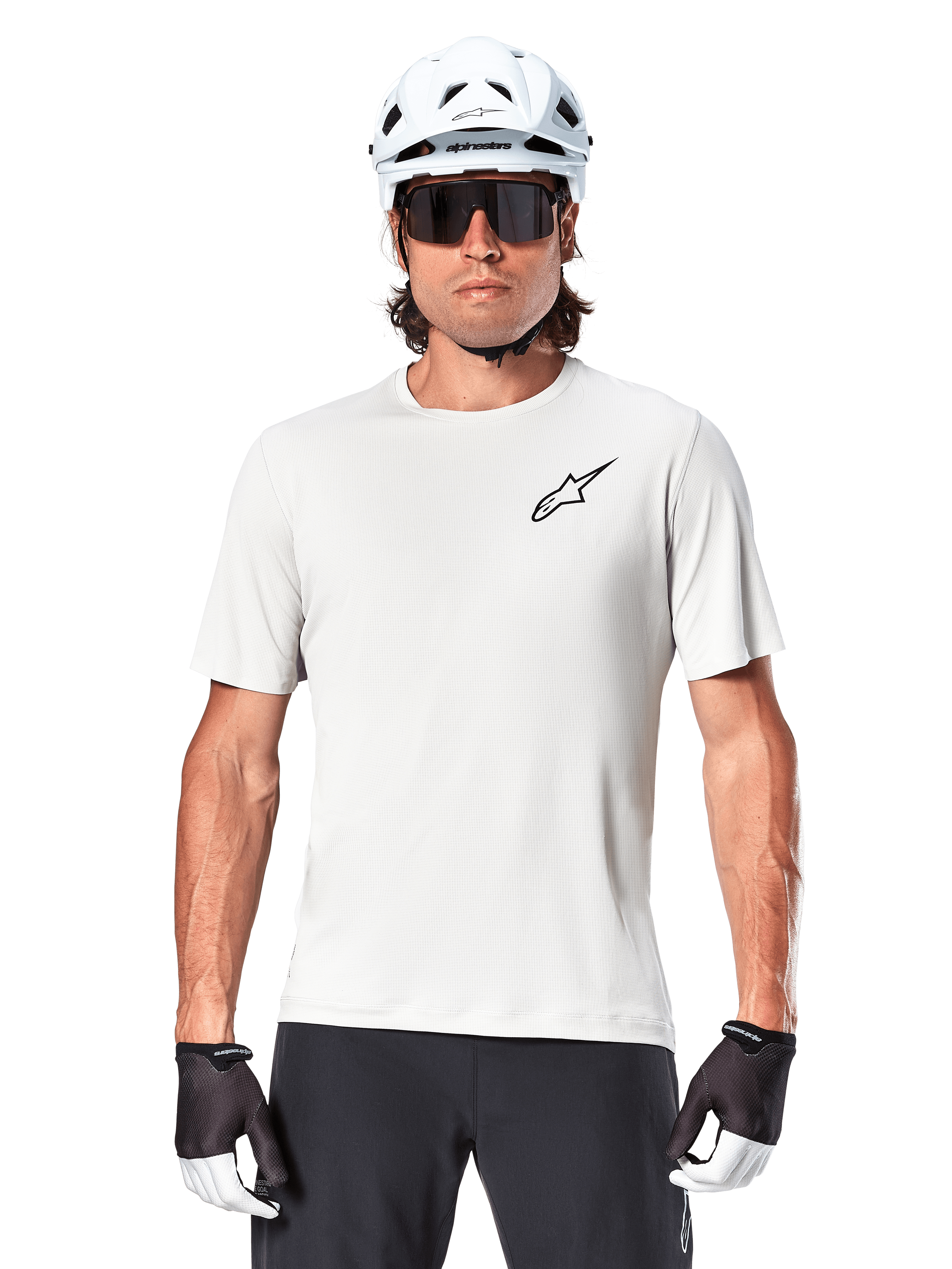 Radfahrer trägt Alpinestars A-Aria Astar Kurzarmtrikot, White Dove mit kleinem schwarzem Astar-Logo auf der Brust, weißer Fahrradhelm, schwarze Sonnenbrille und schwarz-weiße Handschuhe, Performance-MTB-Ausrüstung für Offroad-Fahrten