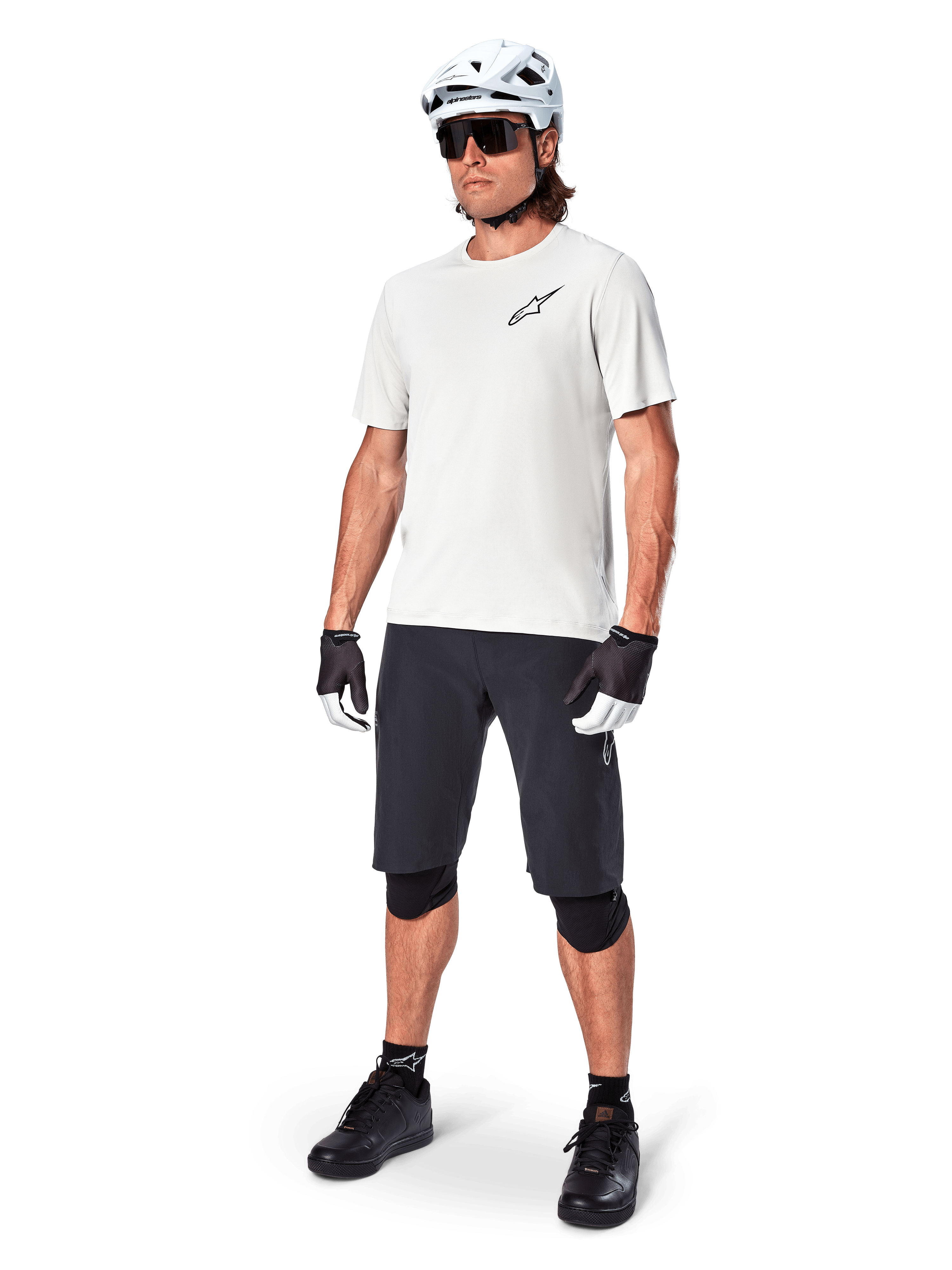 MTB-Fahrer trägt Alpinestars A-Aria Astar Kurzarmtrikot in White Dove, kombiniert mit schwarzen Mountainbike-Shorts, weißem Helm und schwarzen Knieschonern, mit kleinem schwarzen Logo auf der Brust, koordinierte Fahrradausrüstung für Trail-Performance