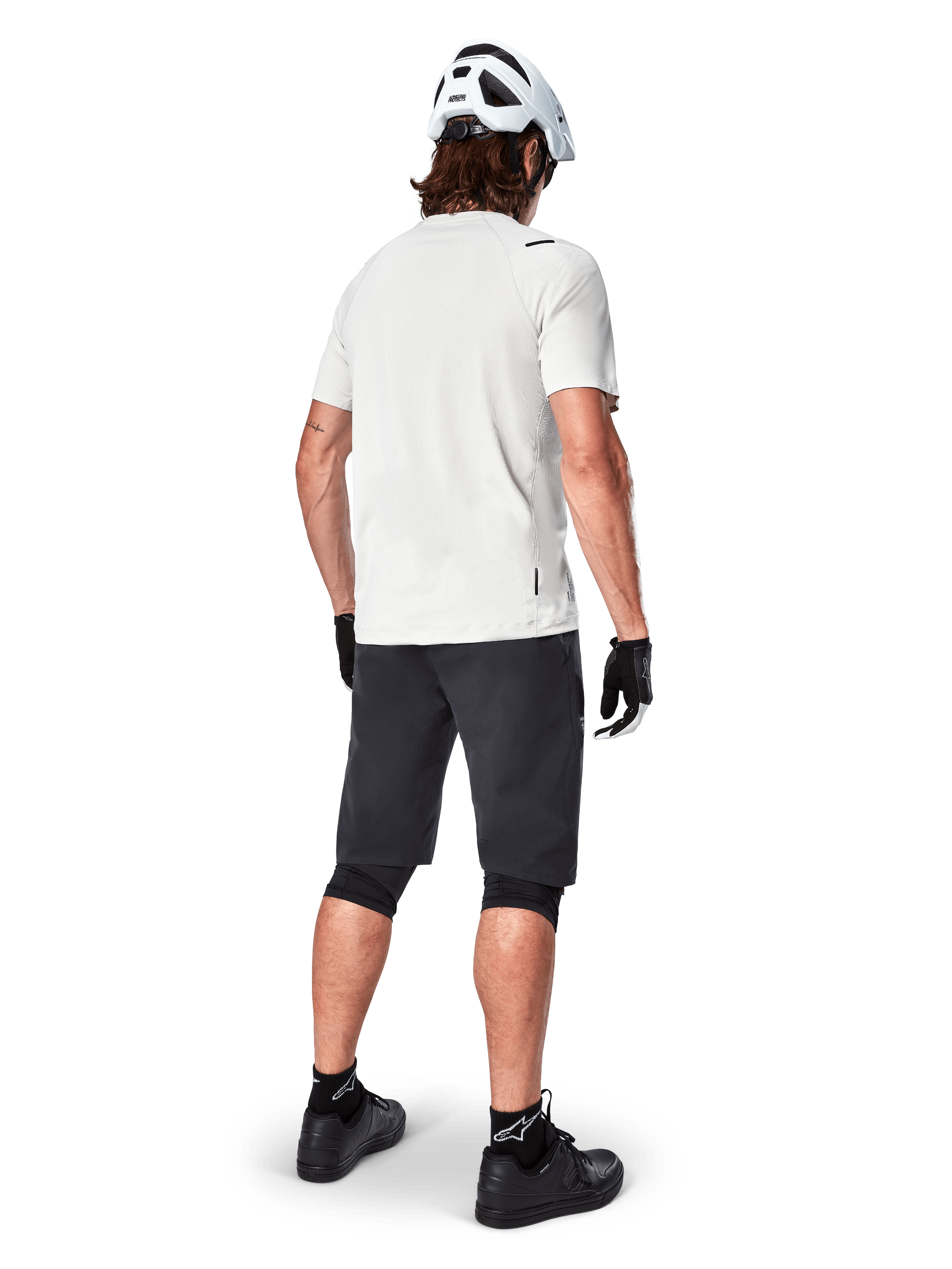 Radfahrer im Alpinestars A-Aria Astar Kurzarmtrikot in White Dove, Rückansicht, kombiniert mit schwarzen MTB-Shorts, Knieschützern und weißem Helm, leichte und atmungsaktive Ausrüstung für das Gelände