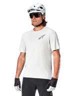 Alpinestars A-Aria Astar Kurzarmtrikot, White Dove, getragen von einem Radfahrer mit weißem Helm und dunkler Sonnenbrille, mit kleinem schwarzem Stern-Logo auf der Brust, atmungsaktive Performance-Ausrüstung für Mountainbiking