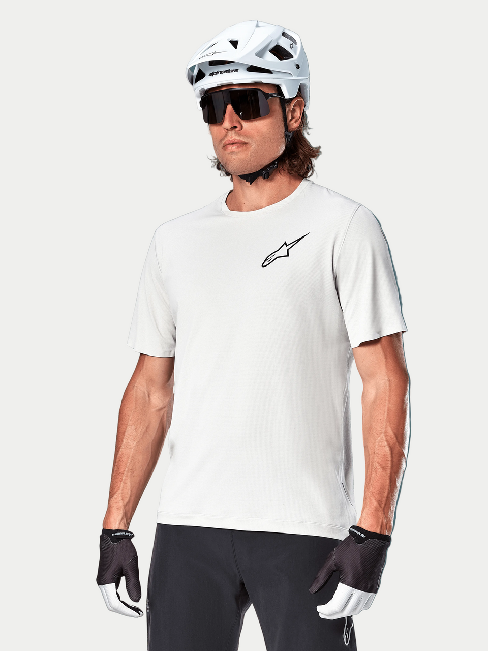 Alpinestars A-Aria Astar Kurzarmtrikot, White Dove, getragen von einem Radfahrer mit weißem Helm und dunkler Sonnenbrille, mit kleinem schwarzem Stern-Logo auf der Brust, atmungsaktive Performance-Ausrüstung für Mountainbiking