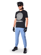 Alpinestars A-Dura Oscar Kurzarmtrikot, schwarzes MTB-Trikot mit einer großen weißen Heritage-Spiralgrafik, getragen von einem Fahrer mit schwarzem Helm, Sonnenbrille, schwarzen Handschuhen und hellblauer Hose, Performance-Mountainbike-Ausrüstung