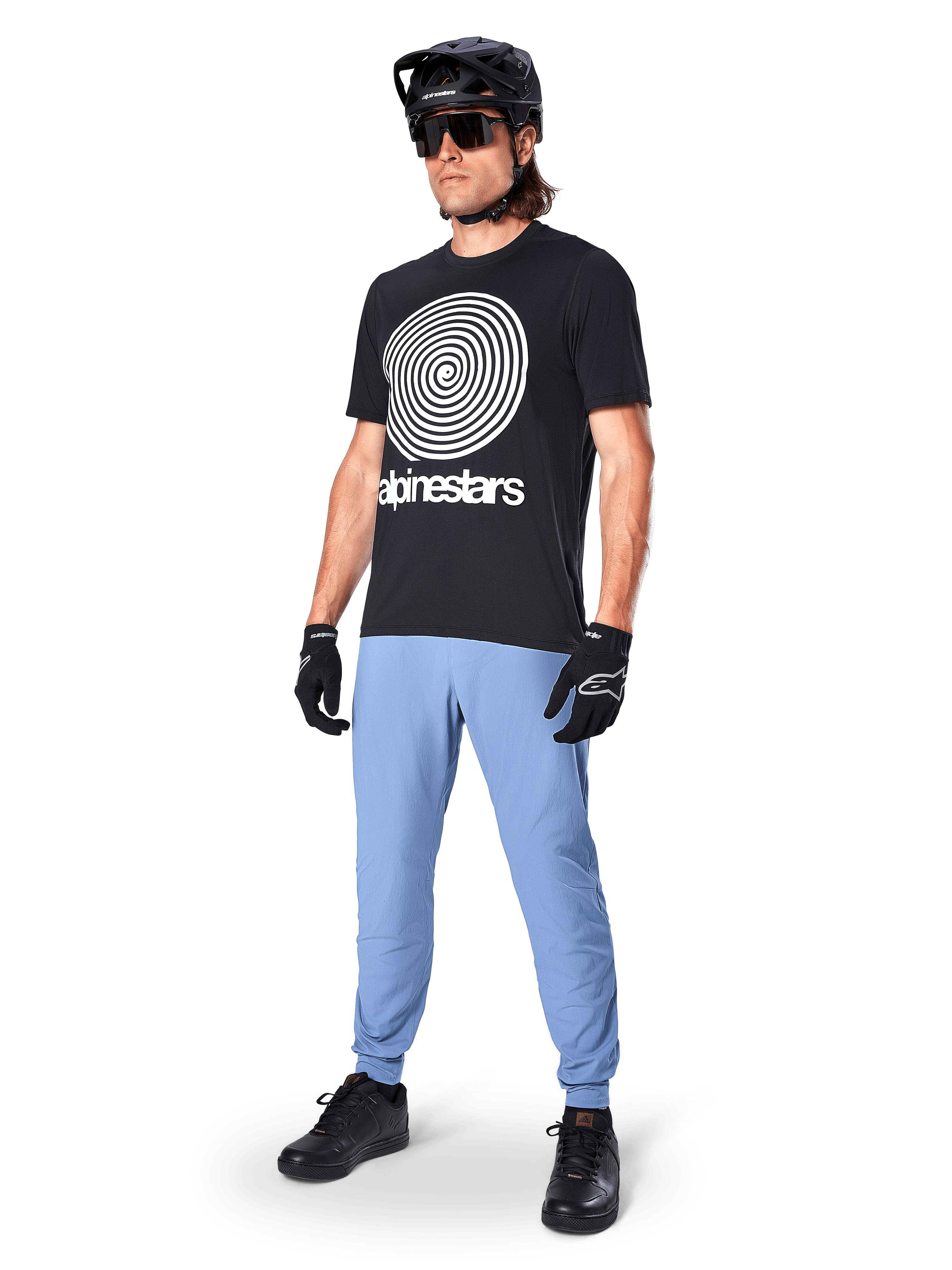 Alpinestars A-Dura Oscar Kurzarmtrikot, schwarzes MTB-Trikot mit einer großen weißen Heritage-Spiralgrafik, getragen von einem Fahrer mit schwarzem Helm, Sonnenbrille, schwarzen Handschuhen und hellblauer Hose, Performance-Mountainbike-Ausrüstung