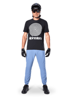 Alpinestars A-Dura Oscar Kurzarmtrikot, schwarzes MTB-Trikot, mit einer großen weißen Vintage-Oscar-Spiralgrafik und Markenschriftzug, getragen mit hellblauer Hose, schwarzem Helm, Sonnenbrille und schwarzen Handschuhen, Performance-Mountainbike-Bekleidung
