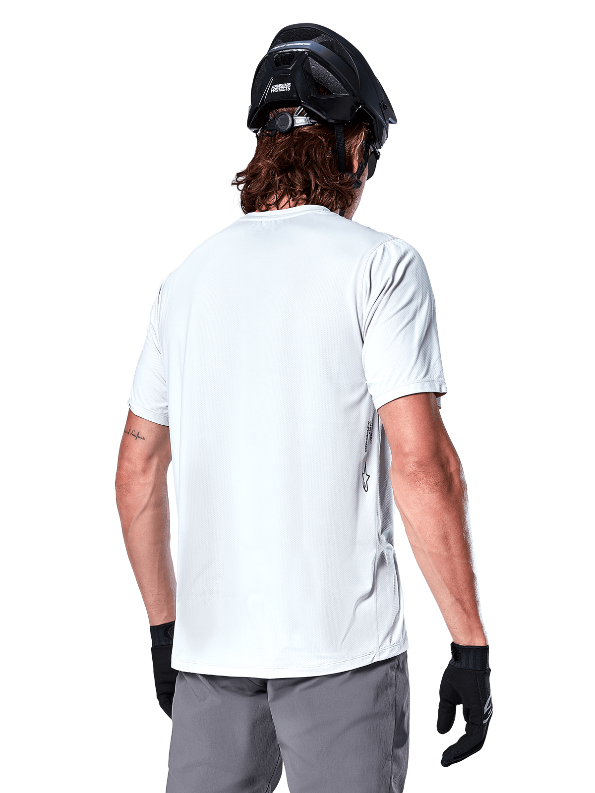 Alpinestars A-Dura Oscar Trikot, Kurzarm-MTB-Trikot, White Dove, Rückansicht eines Fahrers mit schwarzem Fahrradhelm, grauen Shorts und schwarzen Handschuhen, technische Performance-Radsportausrüstung