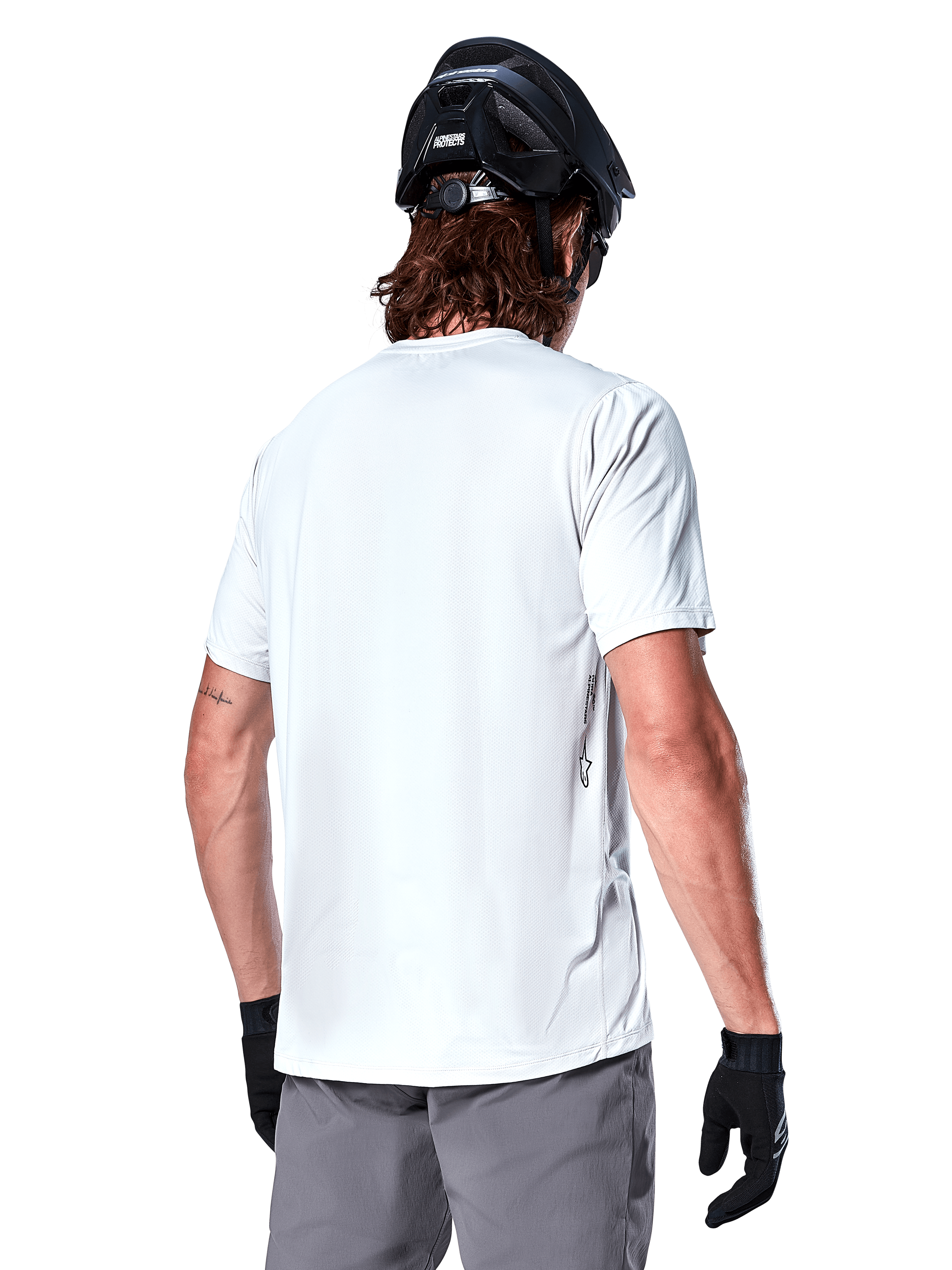 Alpinestars A-Dura Oscar Trikot, Kurzarm-MTB-Trikot, White Dove, Rückansicht eines Fahrers mit schwarzem Fahrradhelm, grauen Shorts und schwarzen Handschuhen, technische Performance-Radsportausrüstung