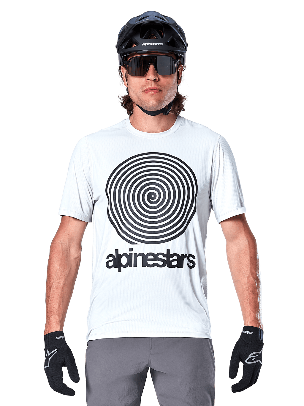 Alpinestars A-Dura Oscar Kurzarmtrikot, White Dove, mit einer großen schwarzen Vintage-Oscar-Spiralgrafik und Alpinestars-Wortmarke auf der Brust, getragen von einem Model mit schwarzem MTB-Helm, Sonnenbrille und schwarzen Handschuhen, Heritage-Radsport-Stil.