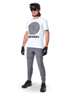 Alpinestars A-Dura Oscar Kurzarmtrikot, White Dove mit großer schwarzer Spiralgrafik, getragen von einem Fahrer mit grauer MTB-Hose, schwarzem Helm und Handschuhen, Performance-Radbekleidung für Geländefahrten