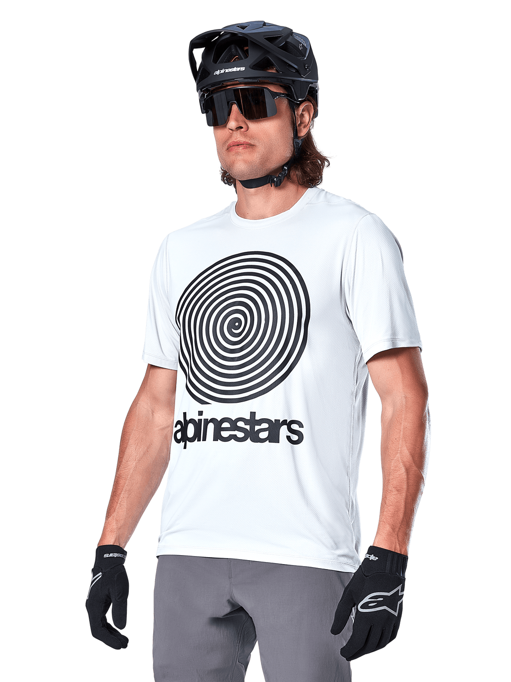 Alpinestars A-Dura Oscar Kurzarmtrikot, White Dove mit schwarzer Heritage-Spiralgrafik und Logo, getragen mit schwarzem MTB-Helm und Handschuhen, sportliche Performance-Mountainbike-Bekleidung