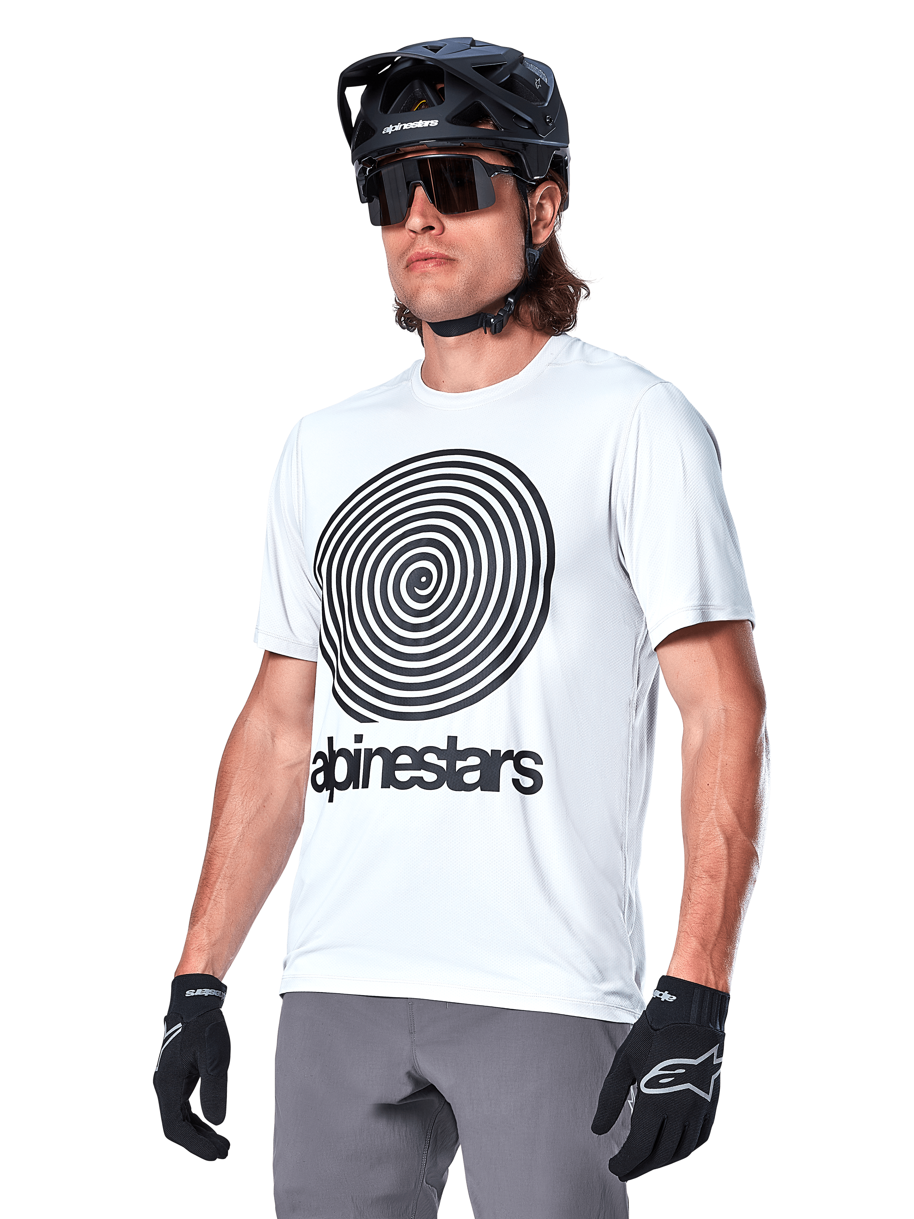 Alpinestars A-Dura Oscar Kurzarmtrikot, White Dove mit schwarzer Heritage-Spiralgrafik und Logo, getragen mit schwarzem MTB-Helm und Handschuhen, sportliche Performance-Mountainbike-Bekleidung