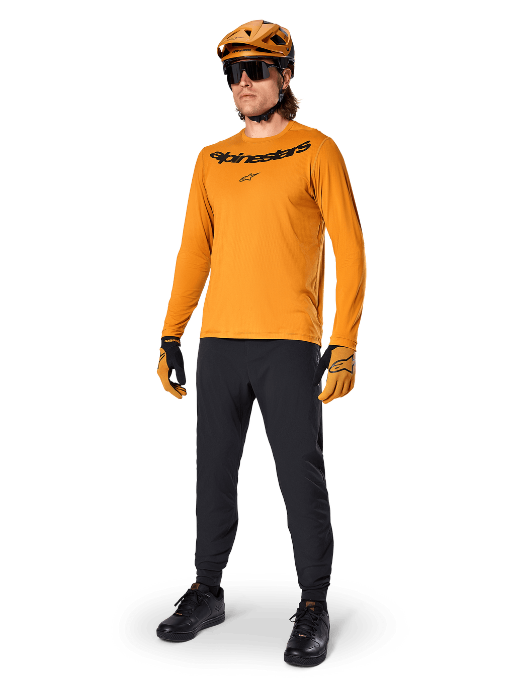 Alpinestars A-Dura Rocker Langarmtrikot, Radsport-Trikot in Dark Gold, getragen mit passendem MTB-Helm und schwarzer Hose, mit schwarzem Wortmarken-Logo auf der Brust, abgestimmte Performance-Ausrüstung für Offroad-Mountainbiking