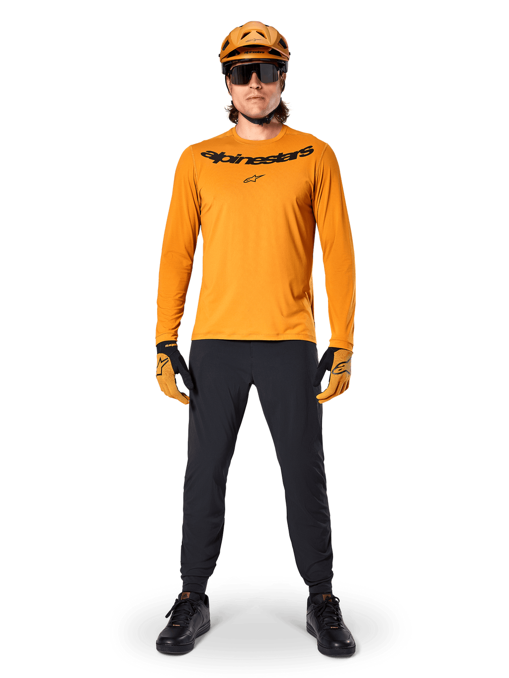 Alpinestars A-Dura Rocker Langarmtrikot in Dark Gold, mit schwarzem Siebdruck-Logo auf der Brust, getragen mit einem passenden goldfarbenen MTB-Helm, schwarzer Sonnenbrille und schwarzer Hose, professionelle Mountainbike-Ausrüstung