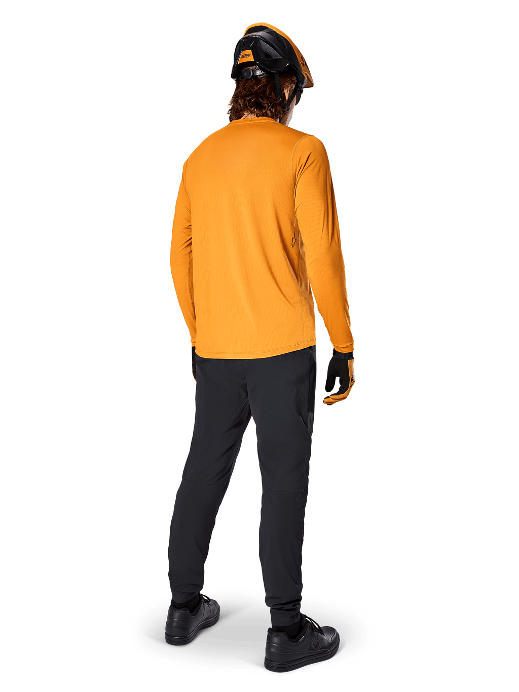 Mountainbike-Fahrer von hinten gesehen im Alpinestars A-Dura Rocker Langarmtrikot in Dark Gold, schwarzer Hose, orange-schwarzem Helm und schwarzen Schuhen, koordinierte Performance-MTB-Ausrüstung für Trailfahrten