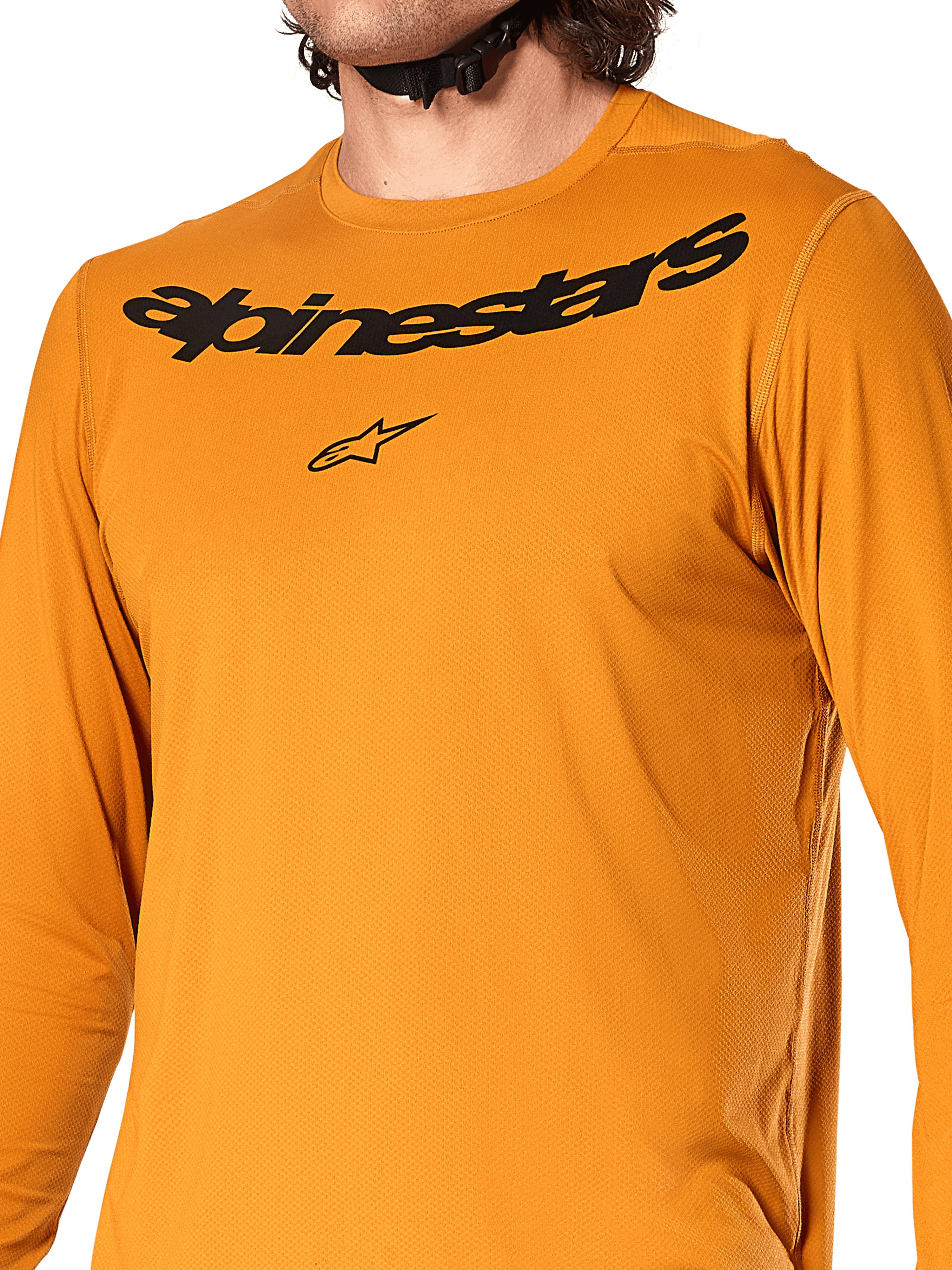 Alpinestars A-Dura Rocker Langarmtrikot, Dunkelgold, Nahaufnahme des Brustbereichs mit schwarzem Alpinestars-Schriftzug und Stern-Logo, strukturiertes feuchtigkeitsableitendes Jacquard-Gewebe, Performance-MTB-Radsportbekleidung