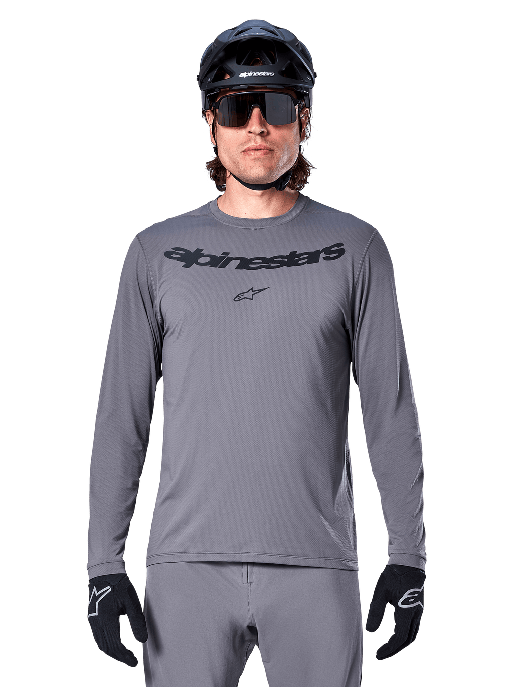 Männlicher Fahrer im Alpinestars A-Dura Rocker Langarmtrikot, dunkelgraues MTB-Trikot mit schwarzem Schriftzug auf der Brust, kombiniert mit grauer Hose, schwarzem Helm und Handschuhen, konzipiert für den Offroad-Radsport