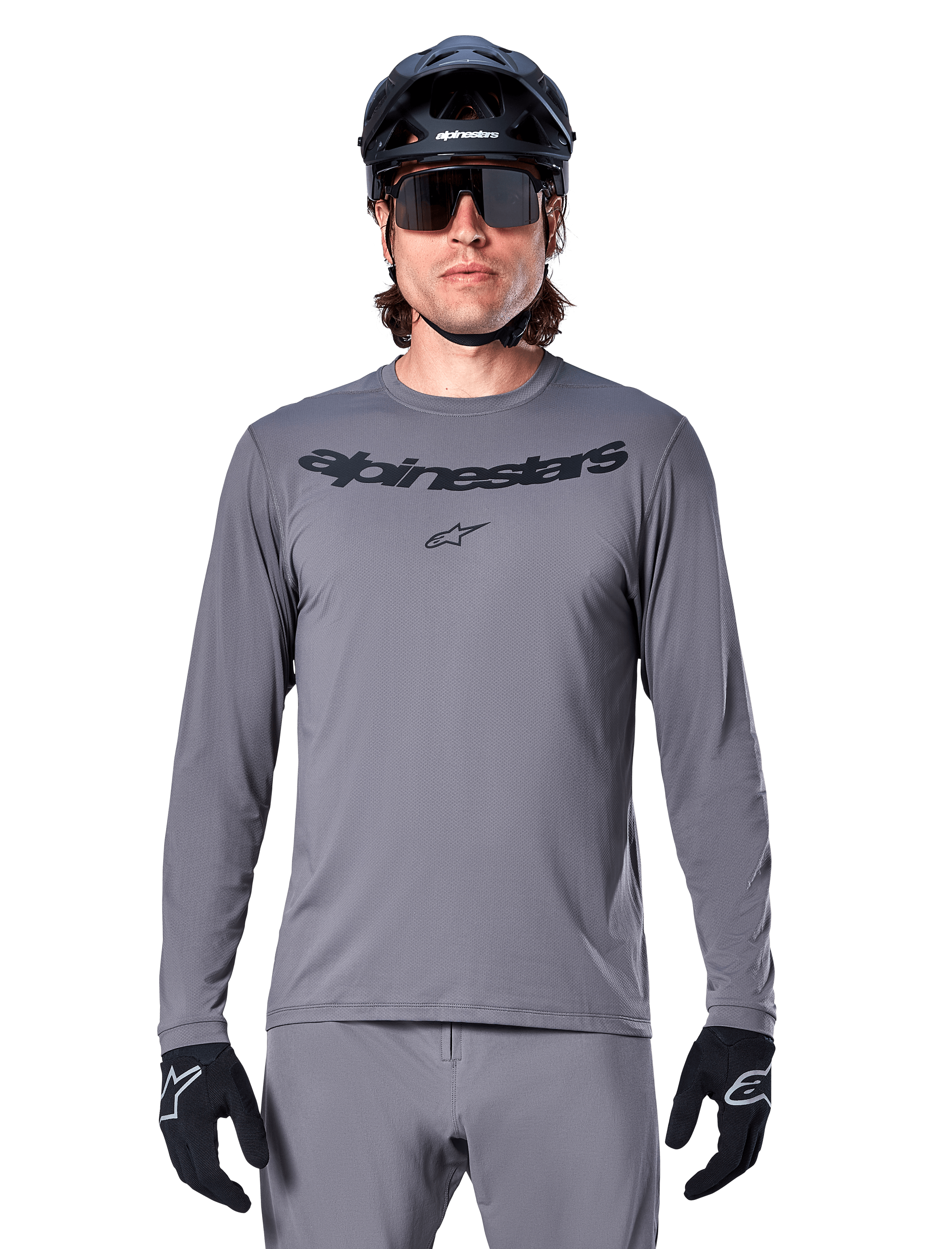 Männlicher Fahrer im Alpinestars A-Dura Rocker Langarmtrikot, dunkelgraues MTB-Trikot mit schwarzem Schriftzug auf der Brust, kombiniert mit grauer Hose, schwarzem Helm und Handschuhen, konzipiert für den Offroad-Radsport