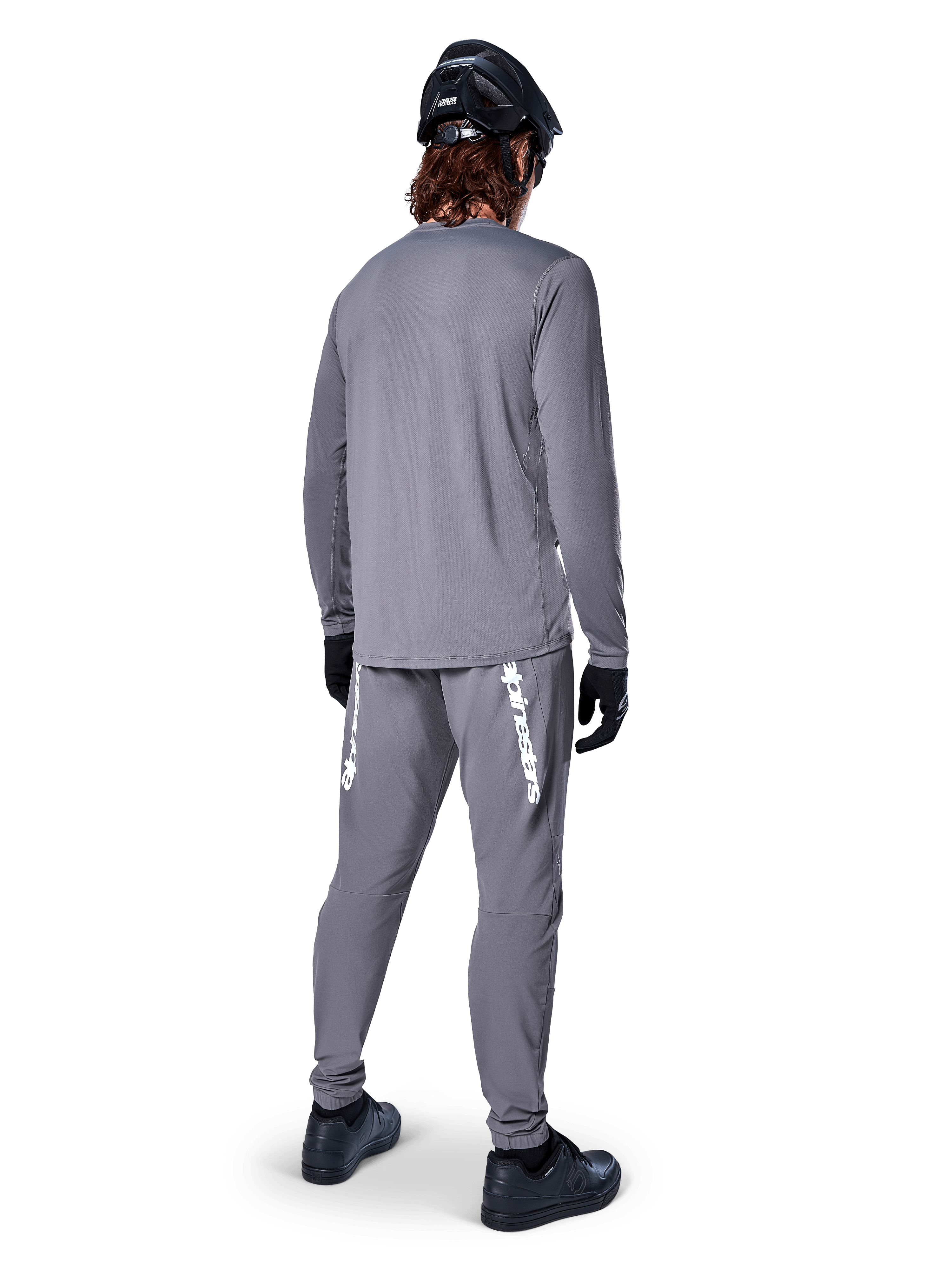 Alpinestars A-Dura Rocker Langarmtrikot, Dunkelgrau, Rückansicht eines Modells mit passender grauer MTB-Hose, schwarzem Helm und schwarzen Handschuhen, professionelles Mountainbike-Bekleidungsdesign