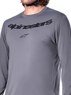 Alpinestars A-Dura Rocker Langarmtrikot, Dunkelgrau, Nahaufnahme der Brust mit schwarzem Alpinestars-Schriftzug und Stern-Logo, Jacquard-Poly-Spandex-Material, Performance-Mountainbike-Bekleidung