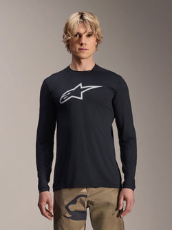Alpinestars A-Dura Astar Langarm-Jersey, Schwarz mit silbernem Astars-Logo auf der Brust, getragen von einem Modell mit Camouflage-Hose, lässige MTB-Performance-Bekleidung für Mountainbiking
