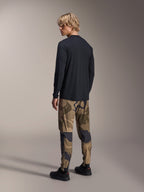 Alpinestars A-Dura Astar Langarmtrikot, Schwarz, Rückansicht an einem Model, kombiniert mit einer Camouflage-Hose, lässige MTB-Performance-Ausrüstung mit verlängertem Rückensaum und regulärer Passform