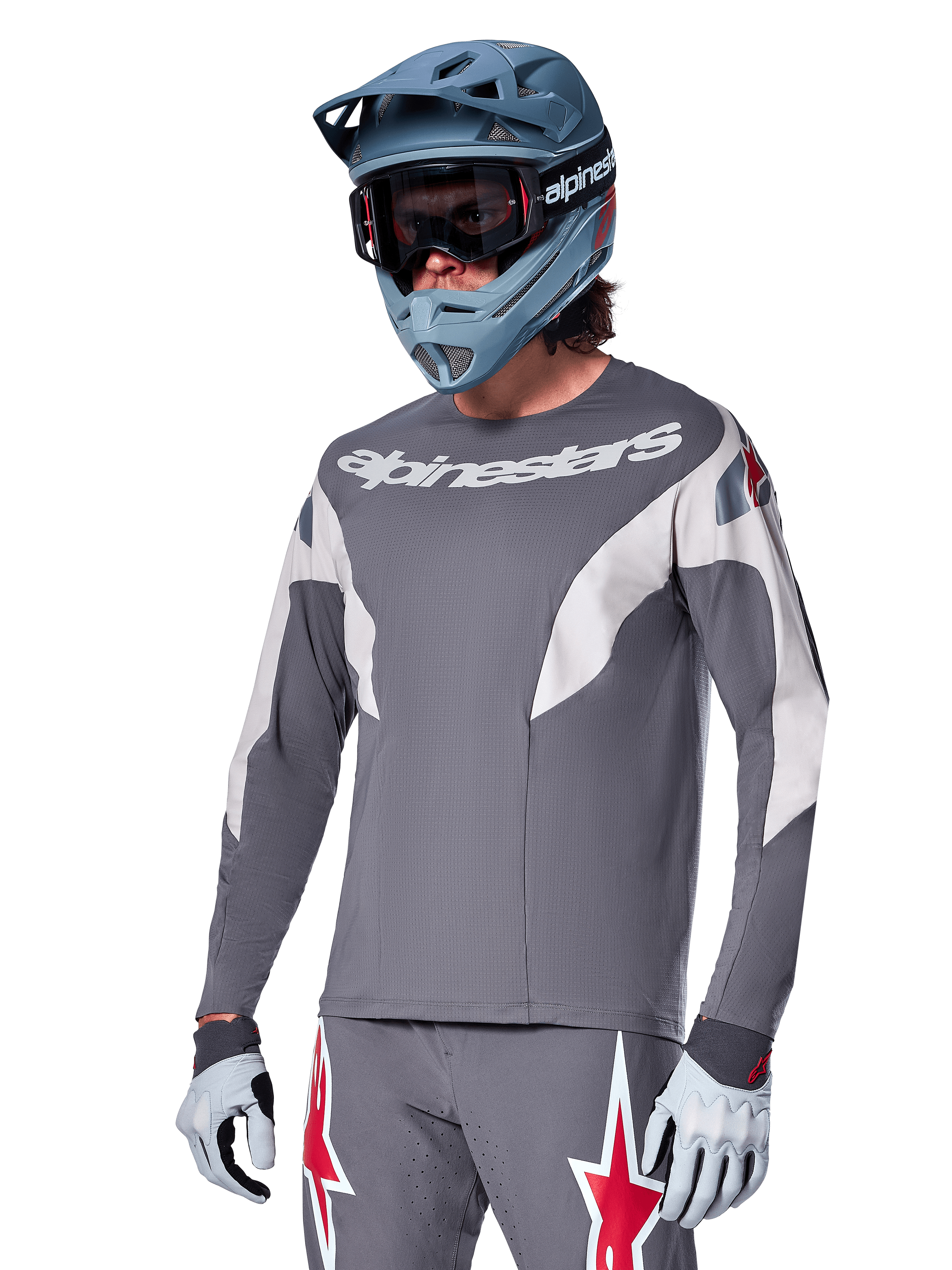 Alpinestars A-Supra Race Trikot – Langarm, Dunkelgrau mit weißen und roten Akzenten, Grafiken im Rennstil, kombiniert mit passender grauer Hose, blauem Fullface-Helm und weißen Handschuhen, professionelle MTB- und Downhill-Rennausrüstung