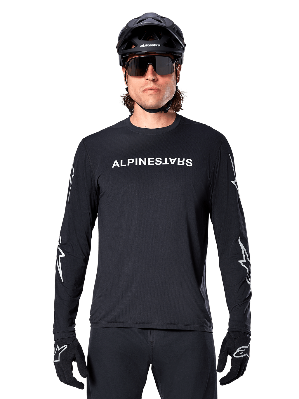 Alpinestars A-Dura Switch Langarmtrikot, schwarzes MTB-Trikot, weißer Alpinestars-Schriftzug auf der Brust und Sterngrafiken auf den Ärmeln, getragen mit schwarzem Mountainbike-Helm und Performance-Sonnenbrille, technische Trail-Bekleidung