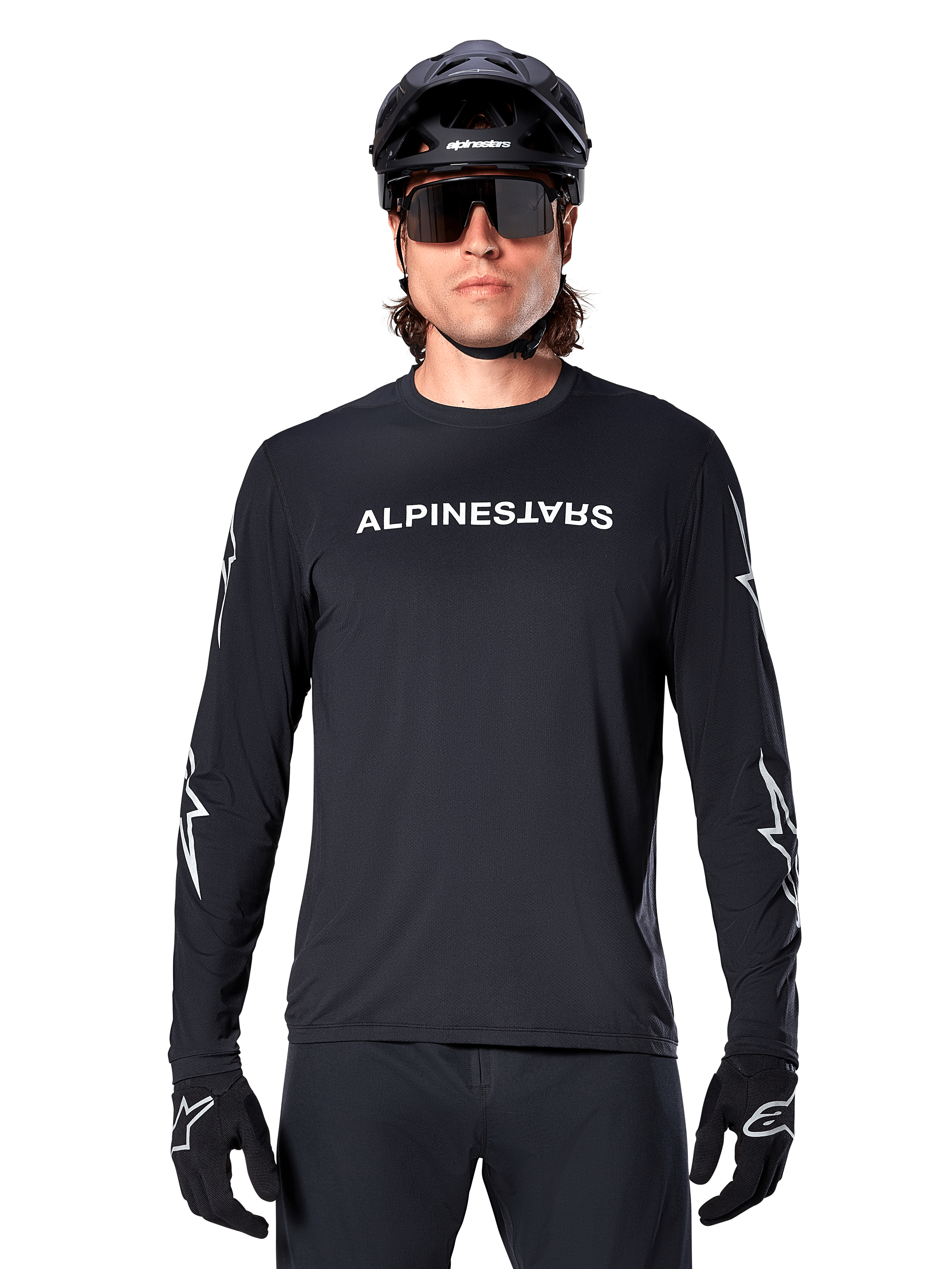 Alpinestars A-Dura Switch Langarmtrikot, schwarzes MTB-Trikot, weißer Alpinestars-Schriftzug auf der Brust und Sterngrafiken auf den Ärmeln, getragen mit schwarzem Mountainbike-Helm und Performance-Sonnenbrille, technische Trail-Bekleidung