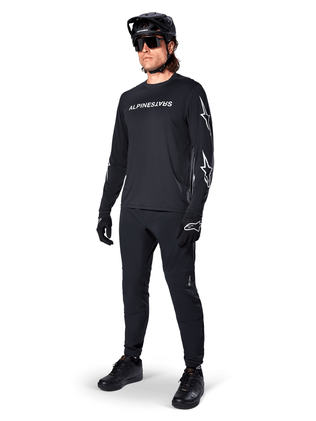 Alpinestars A-Dura Switch Langarmtrikot, Schwarz, Mountainbike-Trikot getragen mit schwarzer Hose, Helm und Handschuhen, mit weißem Wortmarken-Logo auf der Brust und Stern-Logos auf den Ärmeln, abgestimmte MTB-Ausrüstung für Offroad-Fahrten