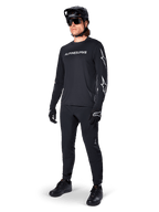 Alpinestars A-Dura Switch Langarmtrikot, Schwarz, Mountainbike-Trikot getragen mit schwarzer Hose, Helm und Handschuhen, mit weißem Wortmarken-Logo auf der Brust und Stern-Logos auf den Ärmeln, abgestimmte MTB-Ausrüstung für Offroad-Fahrten