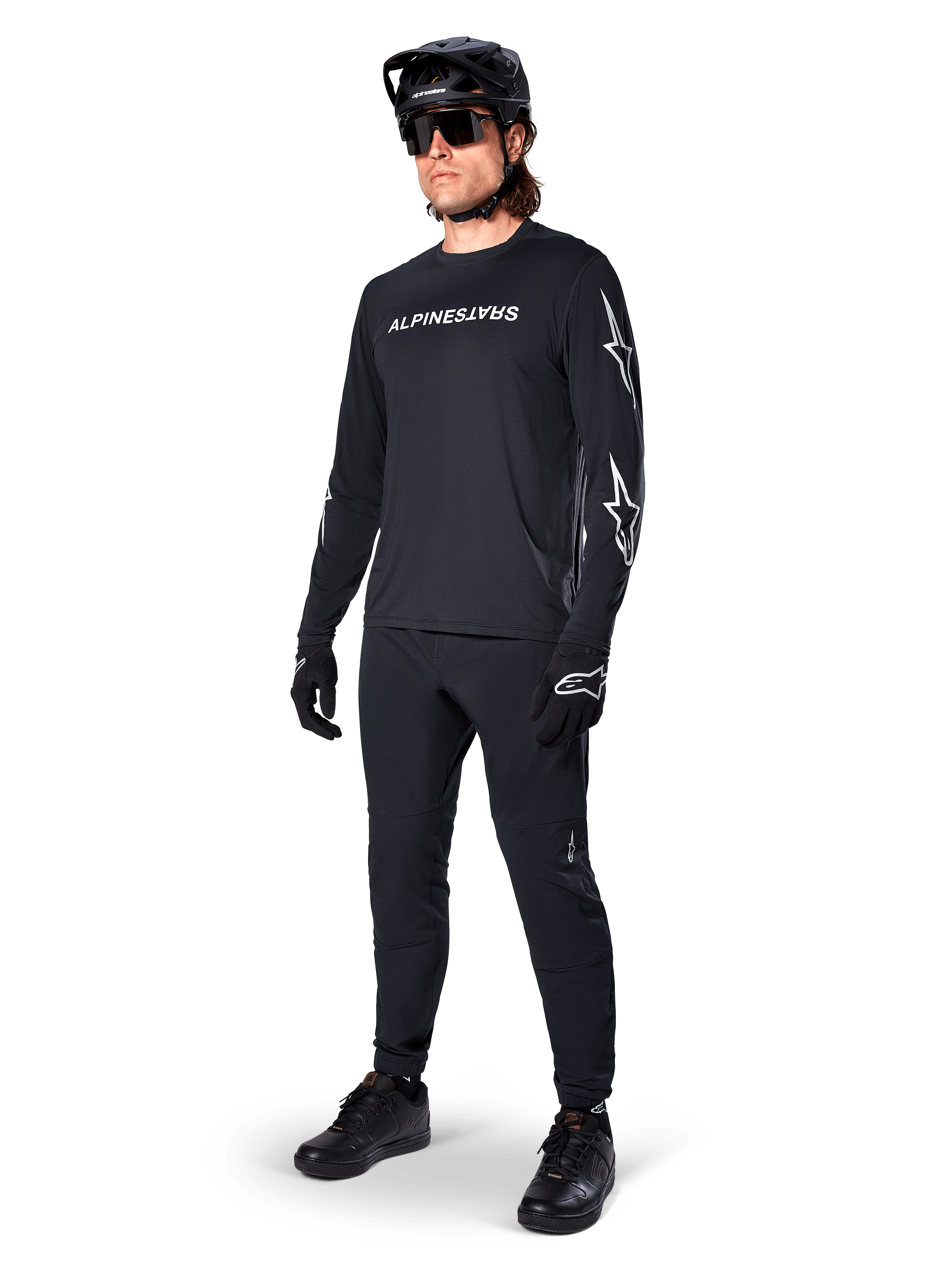 Alpinestars A-Dura Switch Langarmtrikot, Schwarz, Mountainbike-Trikot getragen mit schwarzer Hose, Helm und Handschuhen, mit weißem Wortmarken-Logo auf der Brust und Stern-Logos auf den Ärmeln, abgestimmte MTB-Ausrüstung für Offroad-Fahrten