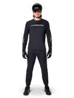 Alpinestars A-Dura Switch Langarmtrikot, Schwarz, getragen von einem Mountainbike-Fahrer mit passender schwarzer Hose und Helm, mit weißem Wortmarken-Logo auf der Brust, technische Offroad-Radsportbekleidung