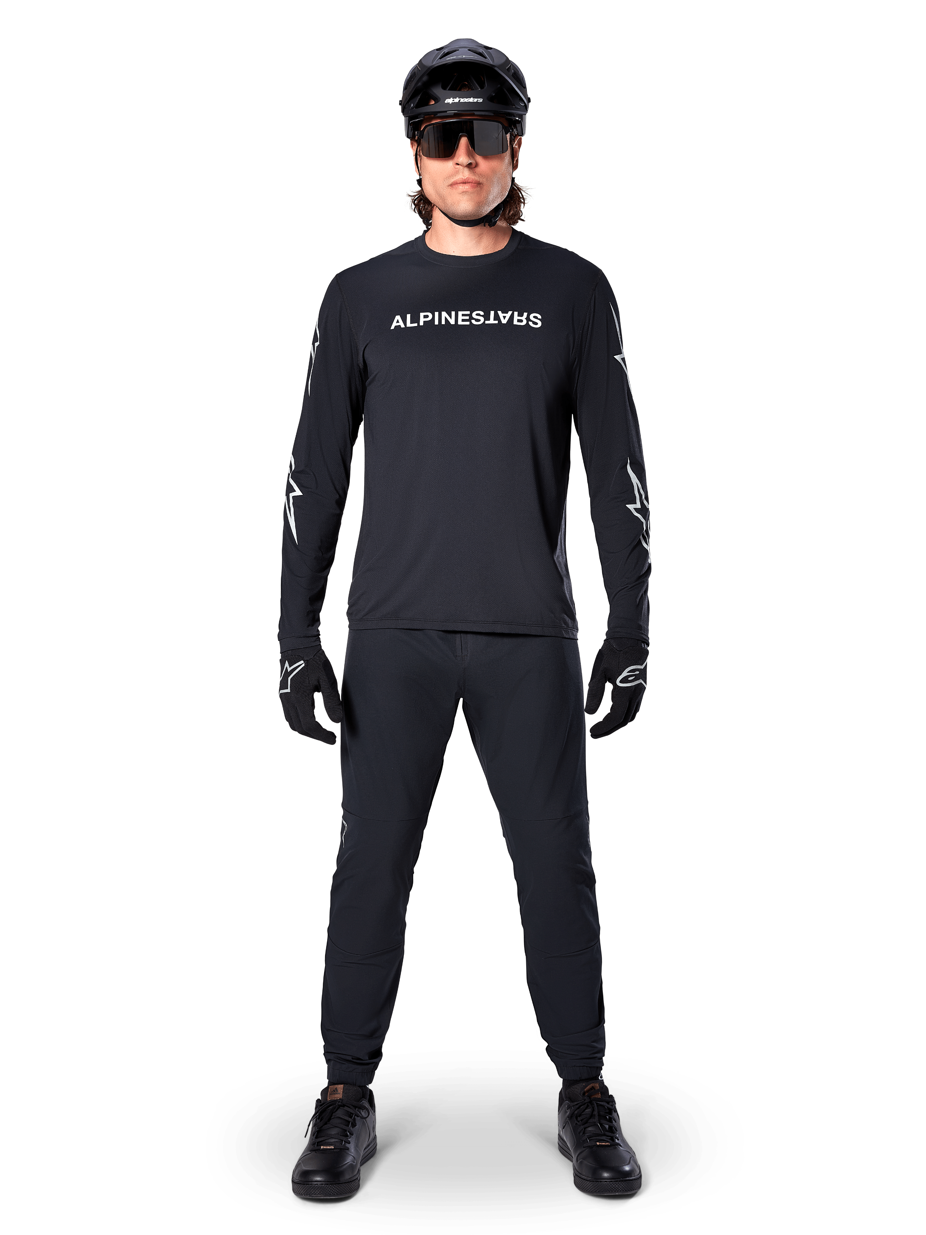 Alpinestars A-Dura Switch Langarmtrikot, Schwarz, getragen von einem Mountainbike-Fahrer mit passender schwarzer Hose und Helm, mit weißem Wortmarken-Logo auf der Brust, technische Offroad-Radsportbekleidung