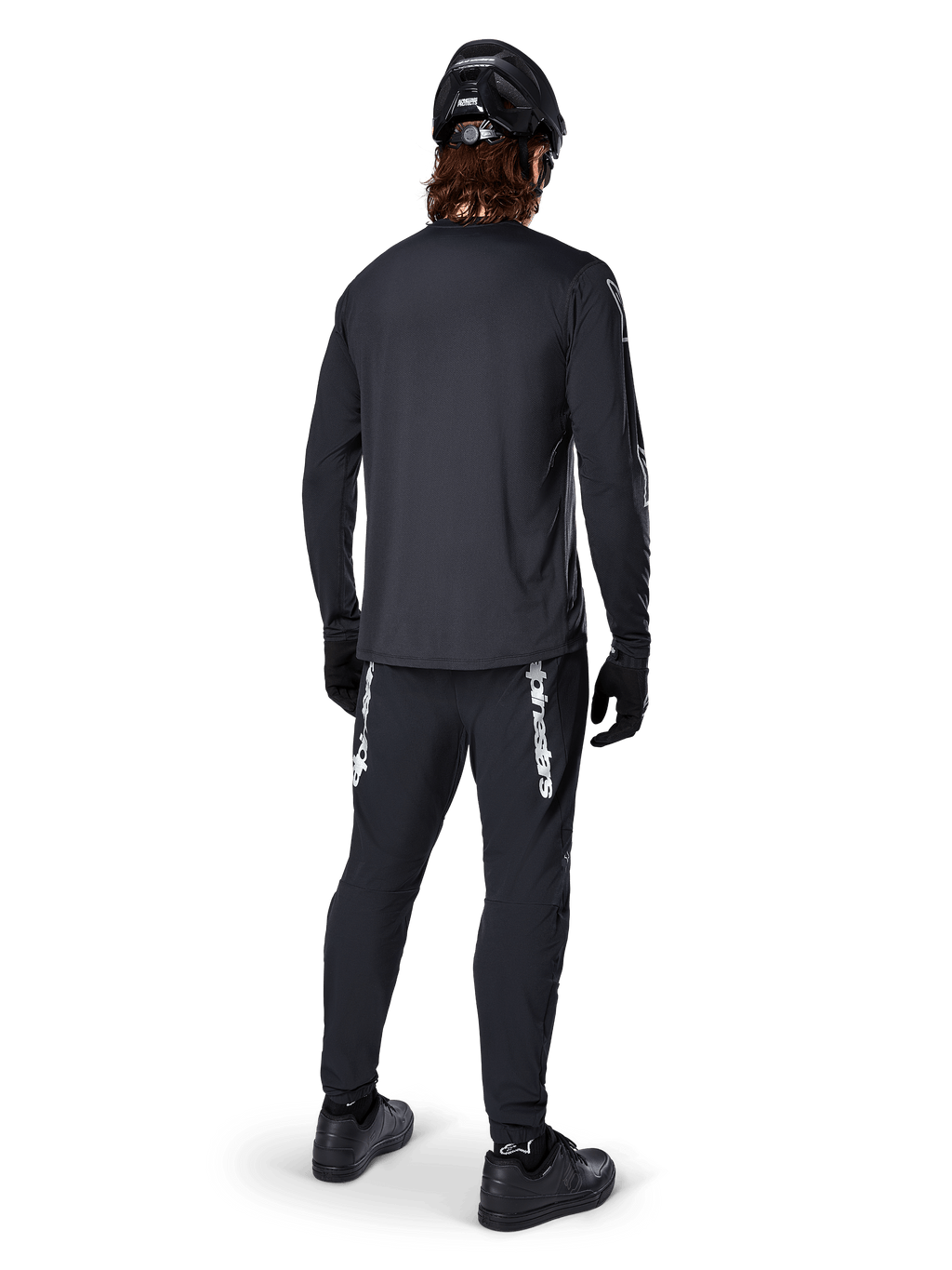 Alpinestars A-Dura Switch Langarmtrikot, Schwarz, Rückansicht an einem Fahrer, getragen mit schwarzer Hose mit weißem Alpinestars-Branding, schwarzem Helm und Handschuhen, mit verlängertem Rückenteil für zusätzliche Abdeckung, Performance-Mountainbike-Bekleidung