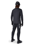 Alpinestars A-Dura Switch Langarmtrikot, Schwarz, Rückansicht an einem Fahrer, getragen mit schwarzer Hose mit weißem Alpinestars-Branding, schwarzem Helm und Handschuhen, mit verlängertem Rückenteil für zusätzliche Abdeckung, Performance-Mountainbike-Bekleidung