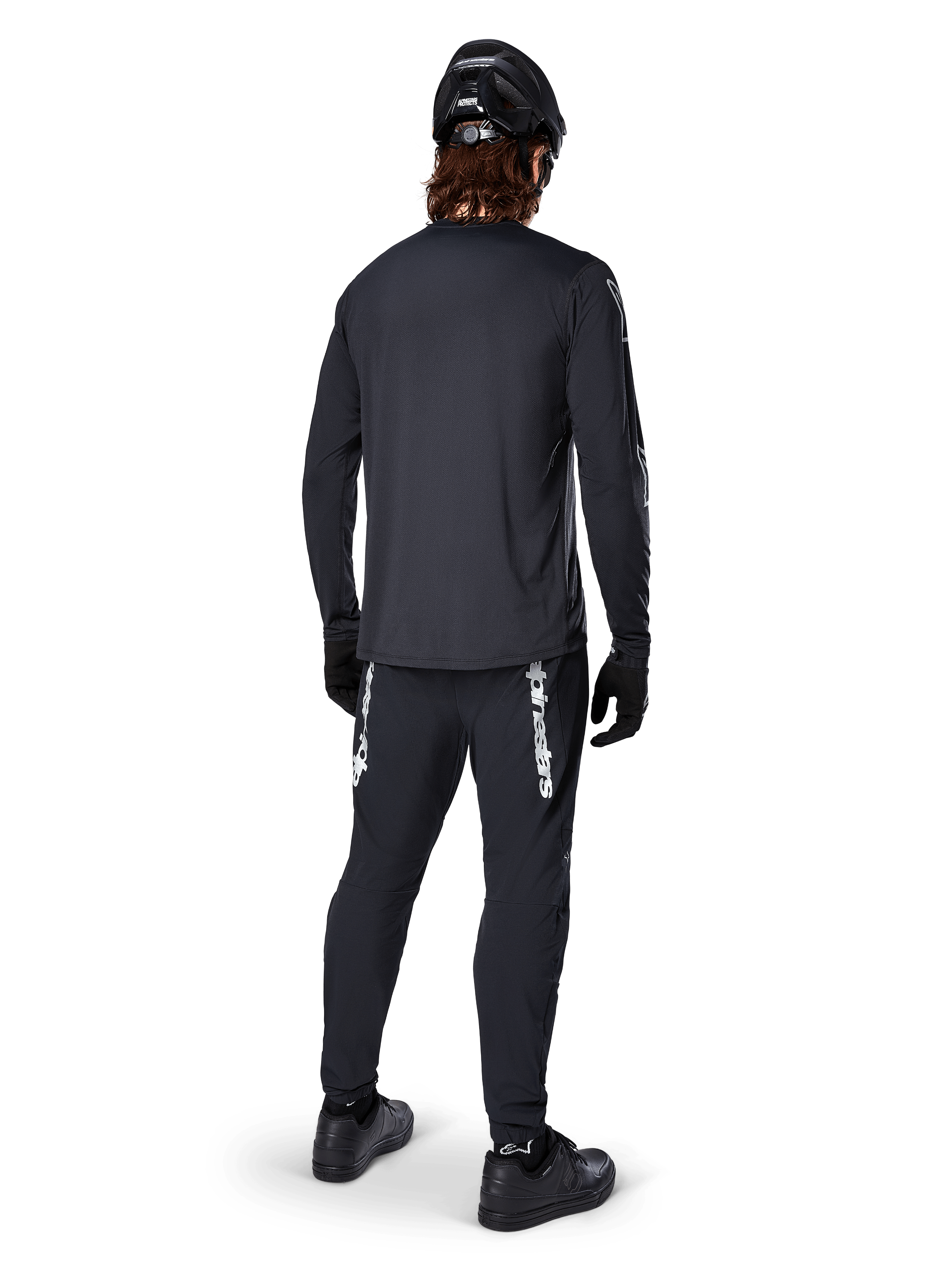 Alpinestars A-Dura Switch Langarmtrikot, Schwarz, Rückansicht an einem Fahrer, getragen mit schwarzer Hose mit weißem Alpinestars-Branding, schwarzem Helm und Handschuhen, mit verlängertem Rückenteil für zusätzliche Abdeckung, Performance-Mountainbike-Bekleidung