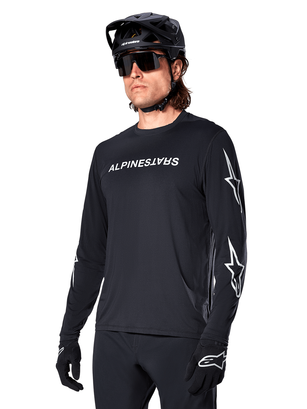 Männlicher Radfahrer im Alpinestars A-Dura Switch Langarmtrikot, Schwarz mit weißem Schriftzug und Stern-Logos auf den Ärmeln, kombiniert mit schwarzem MTB-Helm und Sonnenbrille, Hochleistungs-Radsportausrüstung für Offroad-Fahrten