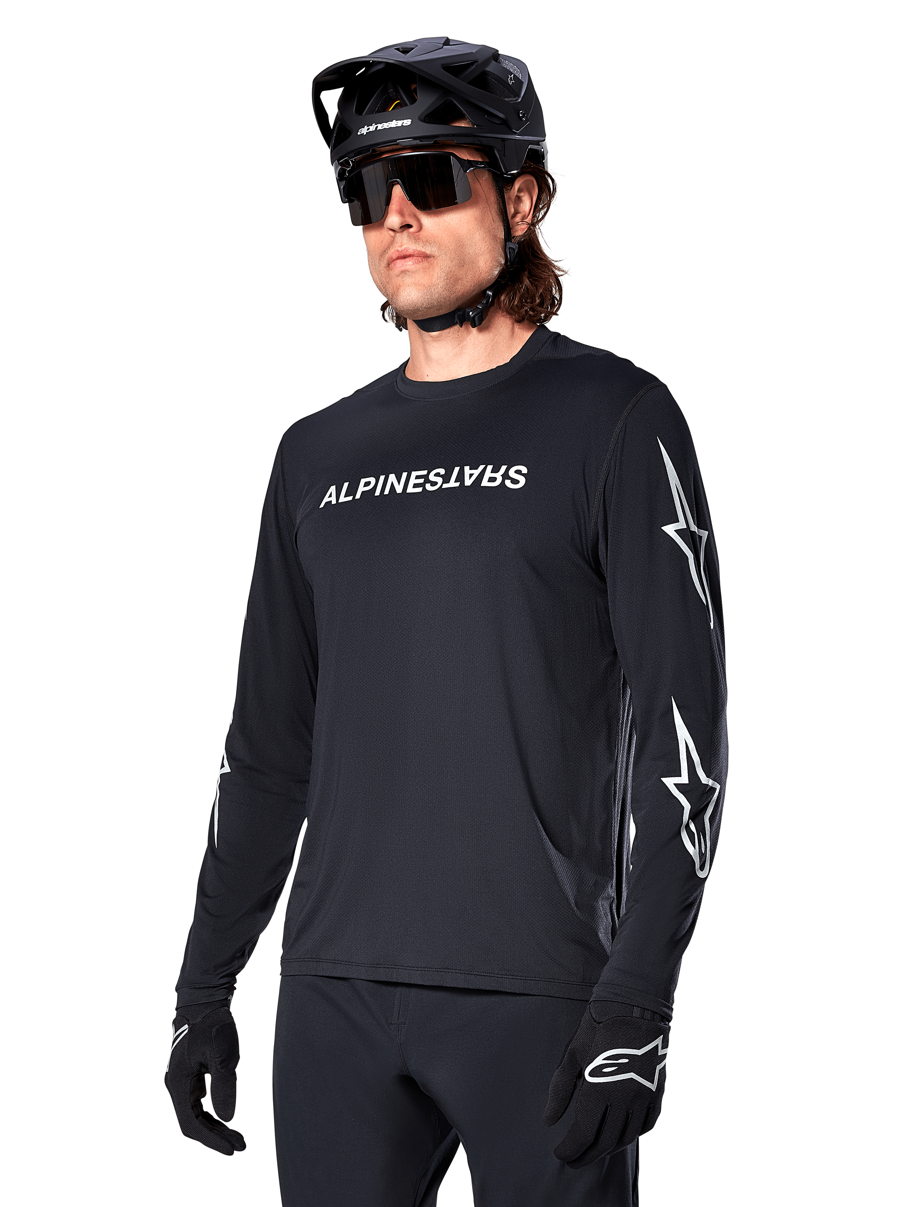 Männlicher Radfahrer im Alpinestars A-Dura Switch Langarmtrikot, Schwarz mit weißem Schriftzug und Stern-Logos auf den Ärmeln, kombiniert mit schwarzem MTB-Helm und Sonnenbrille, Hochleistungs-Radsportausrüstung für Offroad-Fahrten